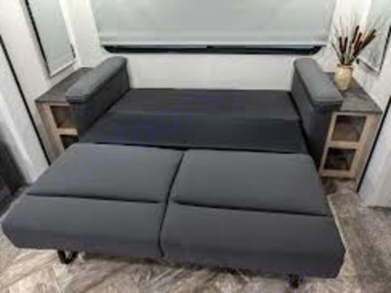 Dark grey convertible sofa bed in an RV rental, unfolded to a sleeping position. Features built-in end tables.. Forest River Palomino Puma 2023