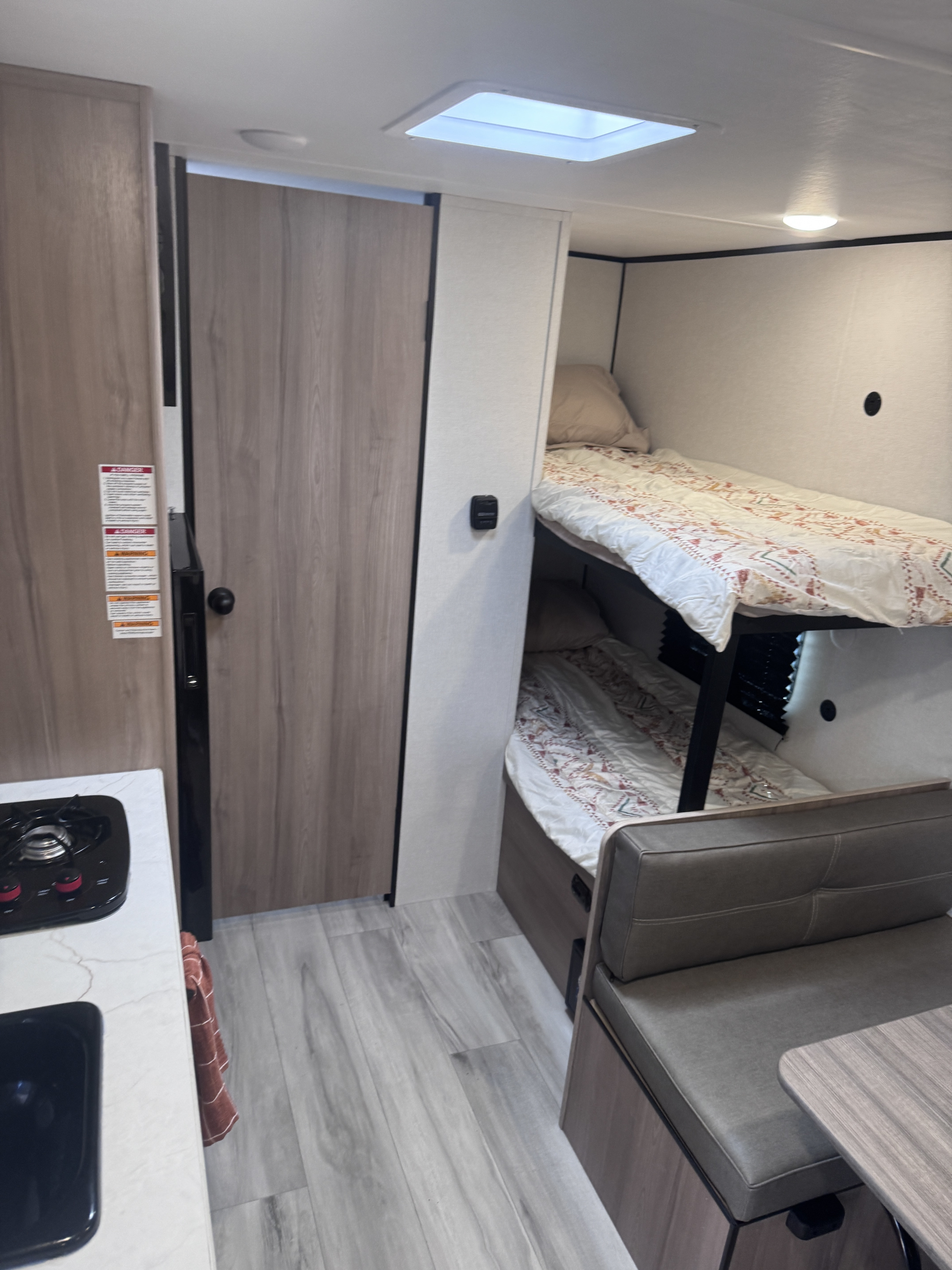 RV rental interior featuring cozy bunk beds, a compact kitchen with stovetop, and a comfortable dinette.. Keystone Coleman 17B 2025