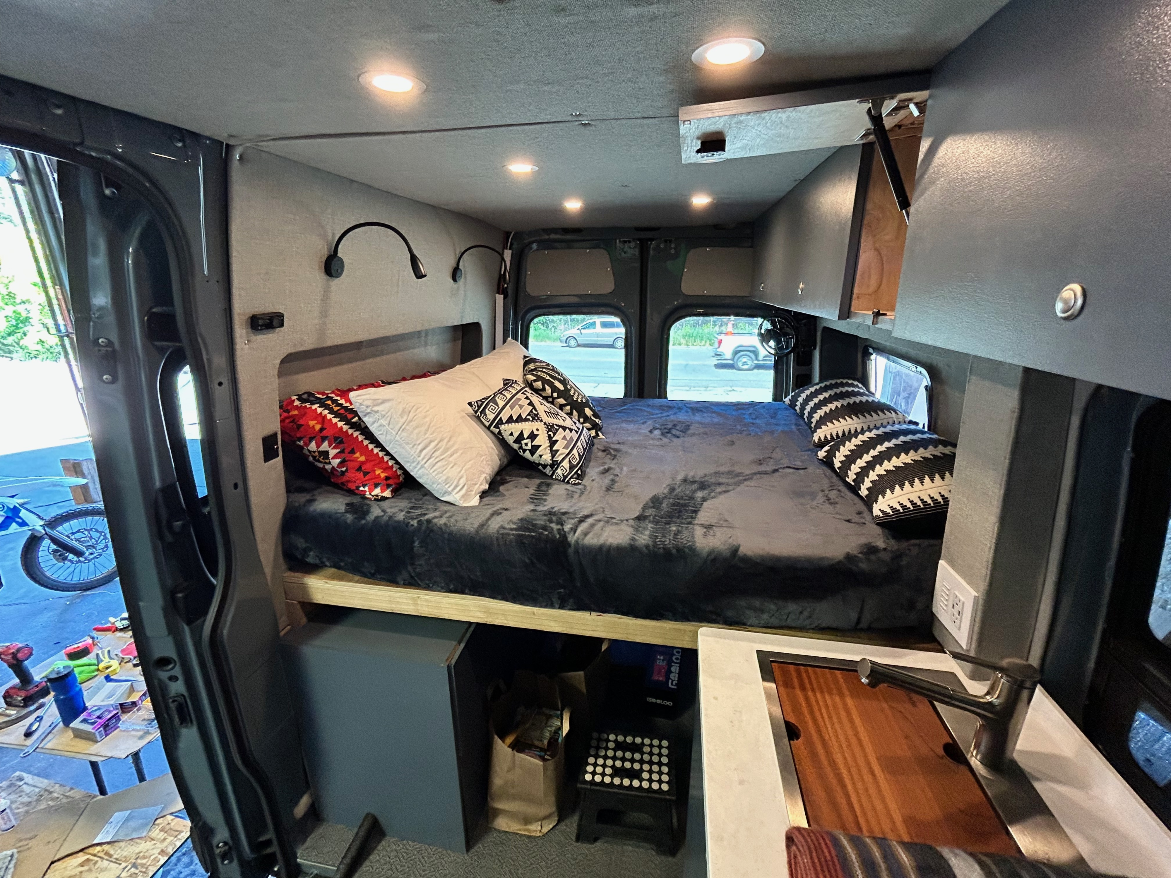This RV rental's cozy interior features a full bed, modern lighting, and a small sink area, ideal for travel.. Mercedes-Benz Sprinter 144 2023