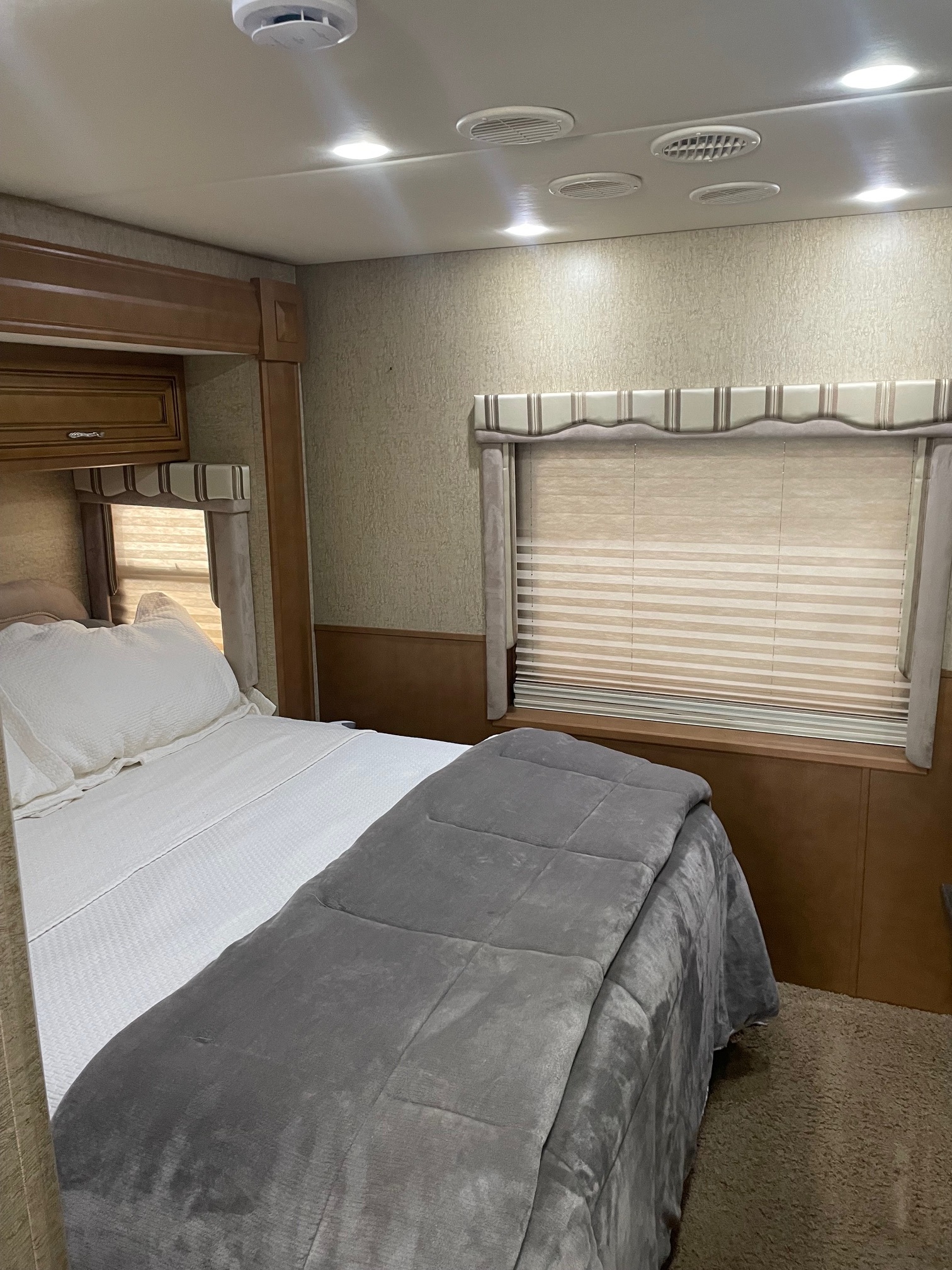Inside a comfortable RV rental bedroom, featuring a neatly made bed, window with blinds, and ceiling with lights/vents.. Newmar Baystar 2012