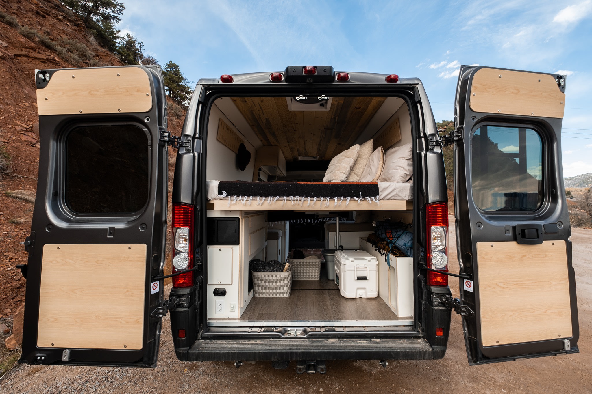 RV rental camper van with open back doors. Built-in bed, storage, and wood paneling reveal a custom interior.. Dodge Ram 1500 2024