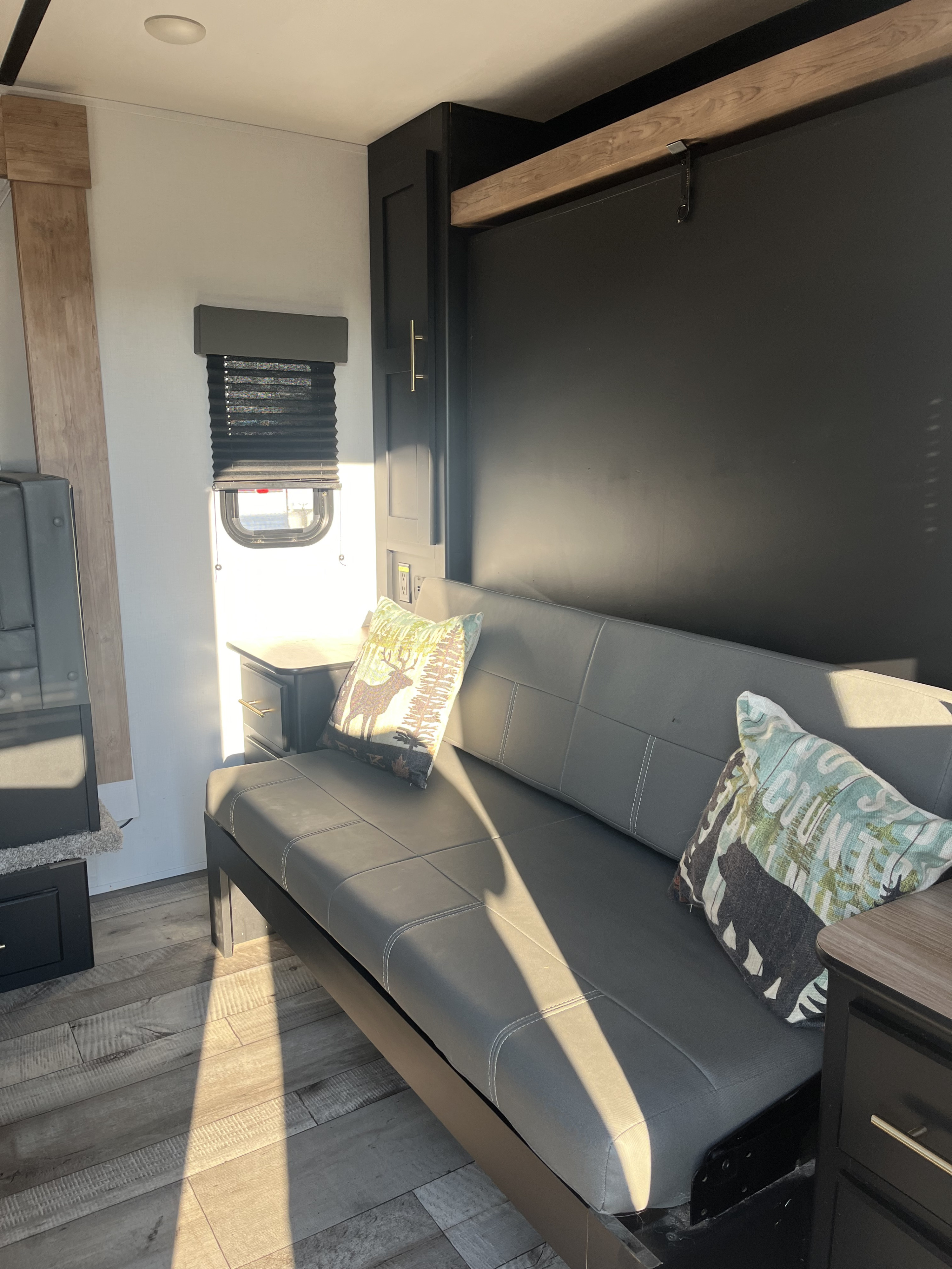 Bright RV rental living space: a gray convertible sofa with decorative pillows, smart storage, and a window with blinds.. Keystone RV Springdale 2022