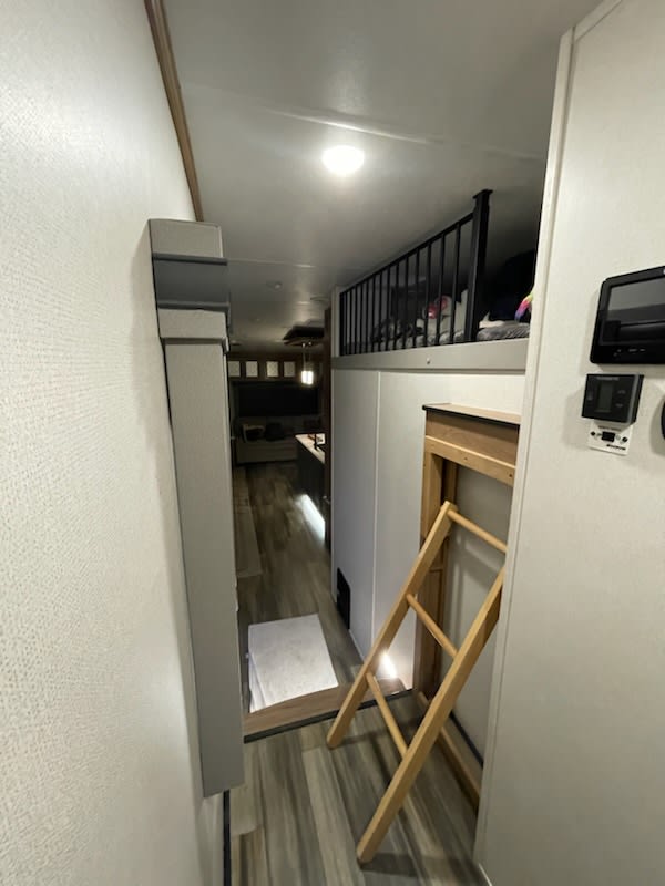 An RV rental interior: view of a hallway leading to a living area, featuring an upper loft bunk with railing and ladder.. Prime Time Sanibel 2022