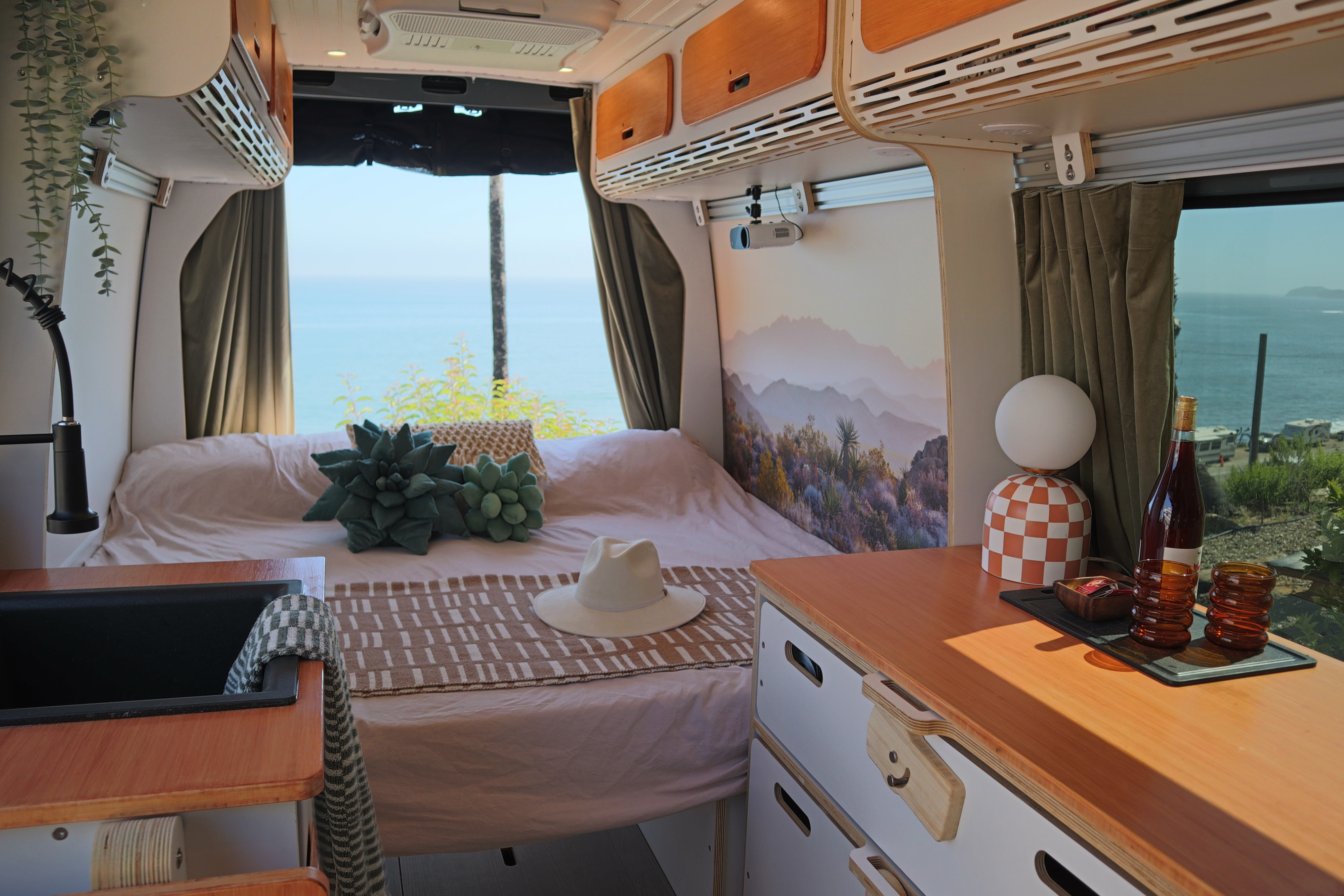 RV rental interior: cozy bed, desert mural, ocean views. Features a kitchen sink, projector & stylish storage for travel.. Mercedes-Benz Sprinter 2022