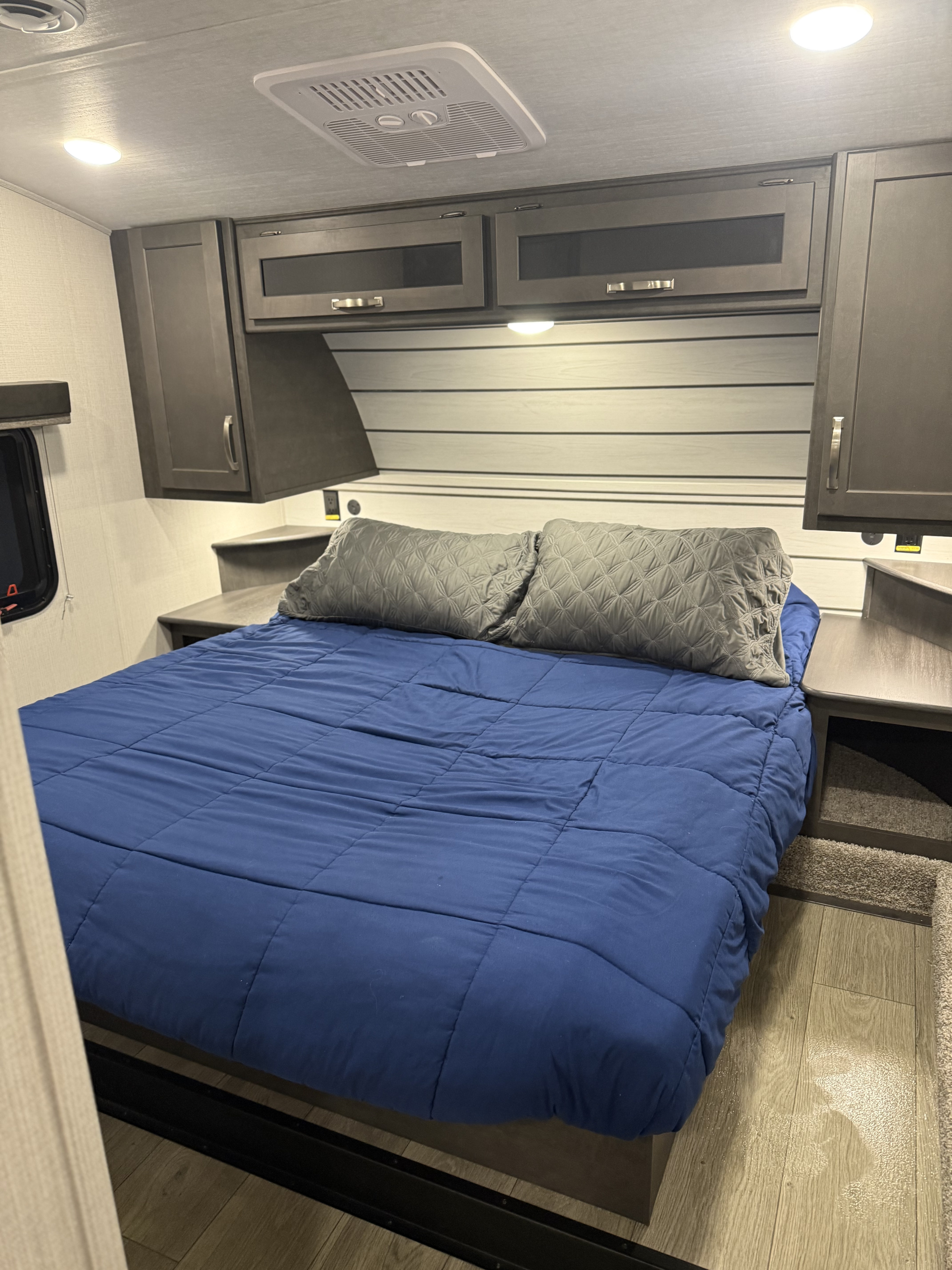 Cozy RV rental bedroom featuring a blue bed, gray pillows, modern overhead cabinets, and ceiling AC unit.. Keystone RV Cougar 2024