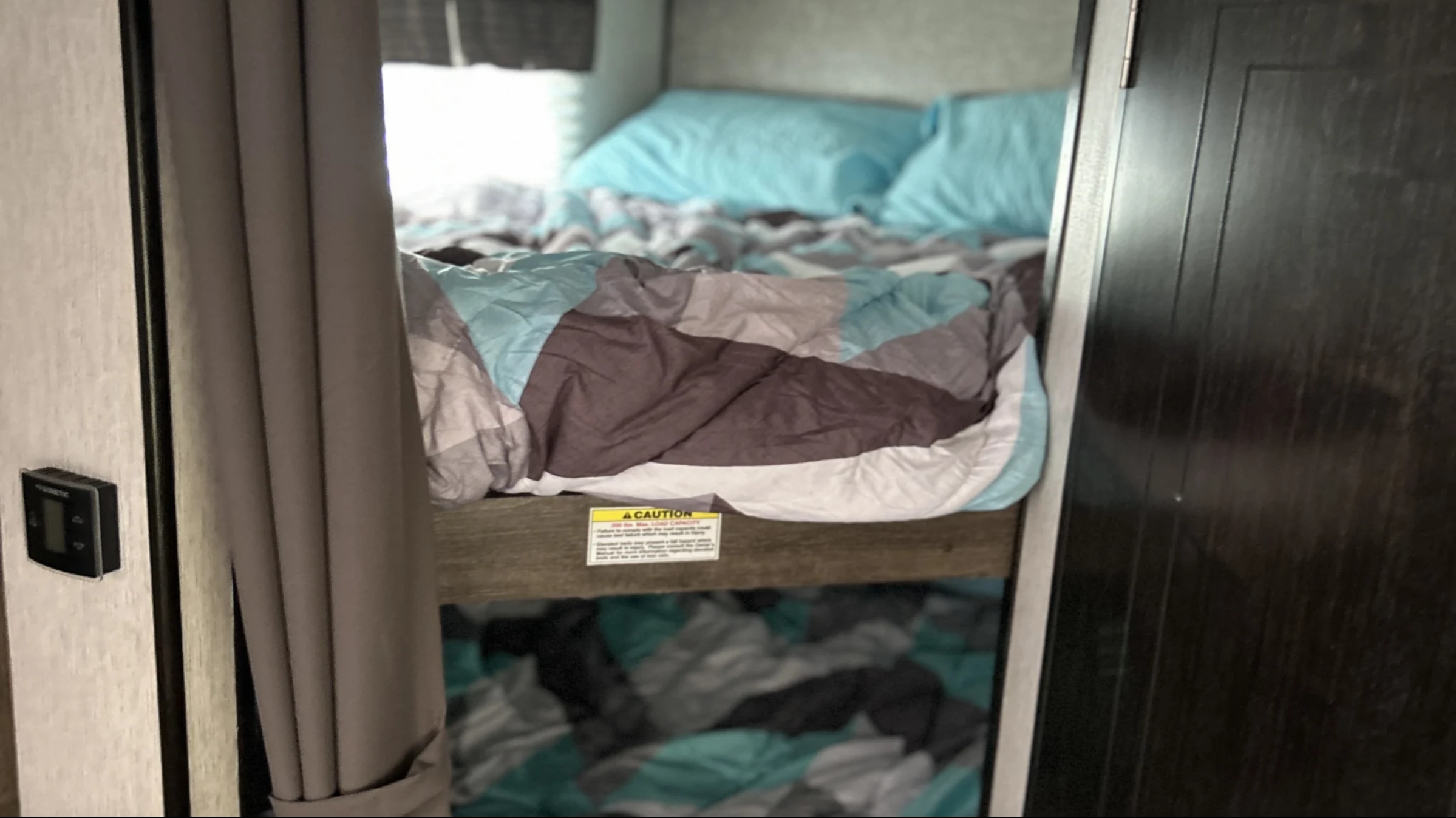 Cozy RV rental bunk beds with patterned bedding (grey, brown, blue). A DOMETIC thermostat and caution sign are visible.. Heartland RVs Mallard 2019