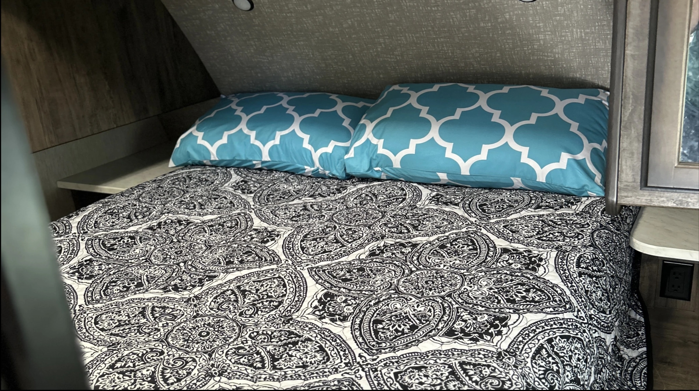 Comfortable RV rental bedroom featuring two aqua blue and white patterned pillows atop a black and white paisley comforter.. Heartland RVs Mallard 2019