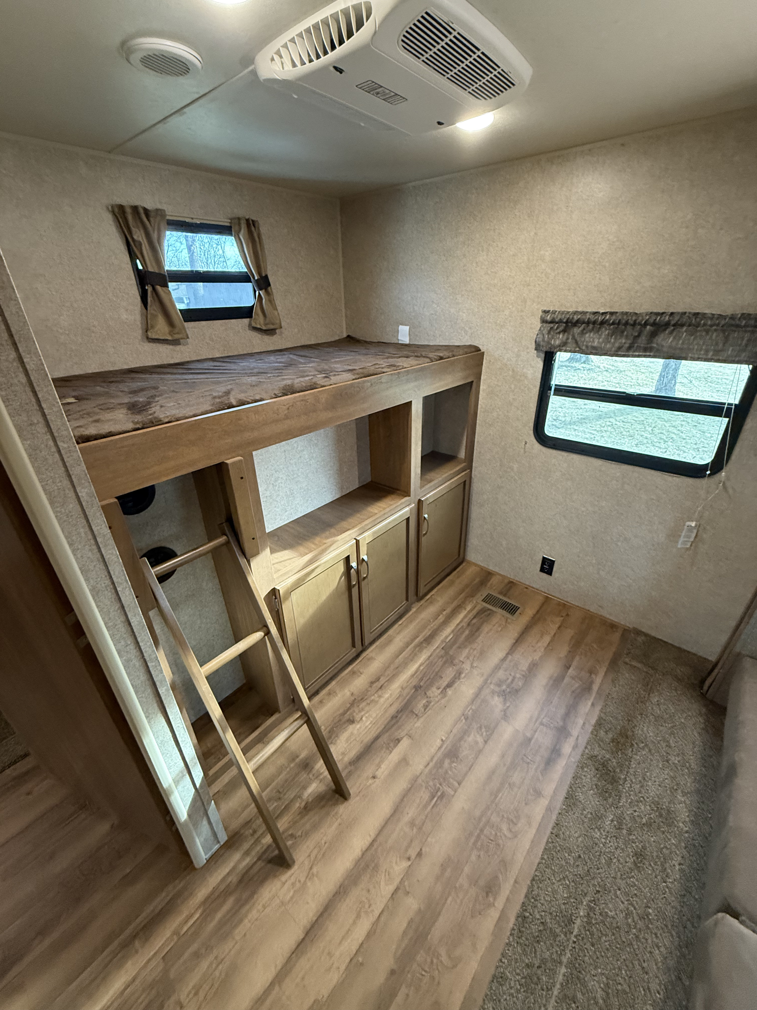 Cozy RV rental interior showing bunk beds, a ladder, built-in storage, windows, and ceiling AC.. Forest River Coachmen Catalina Legacy 2018