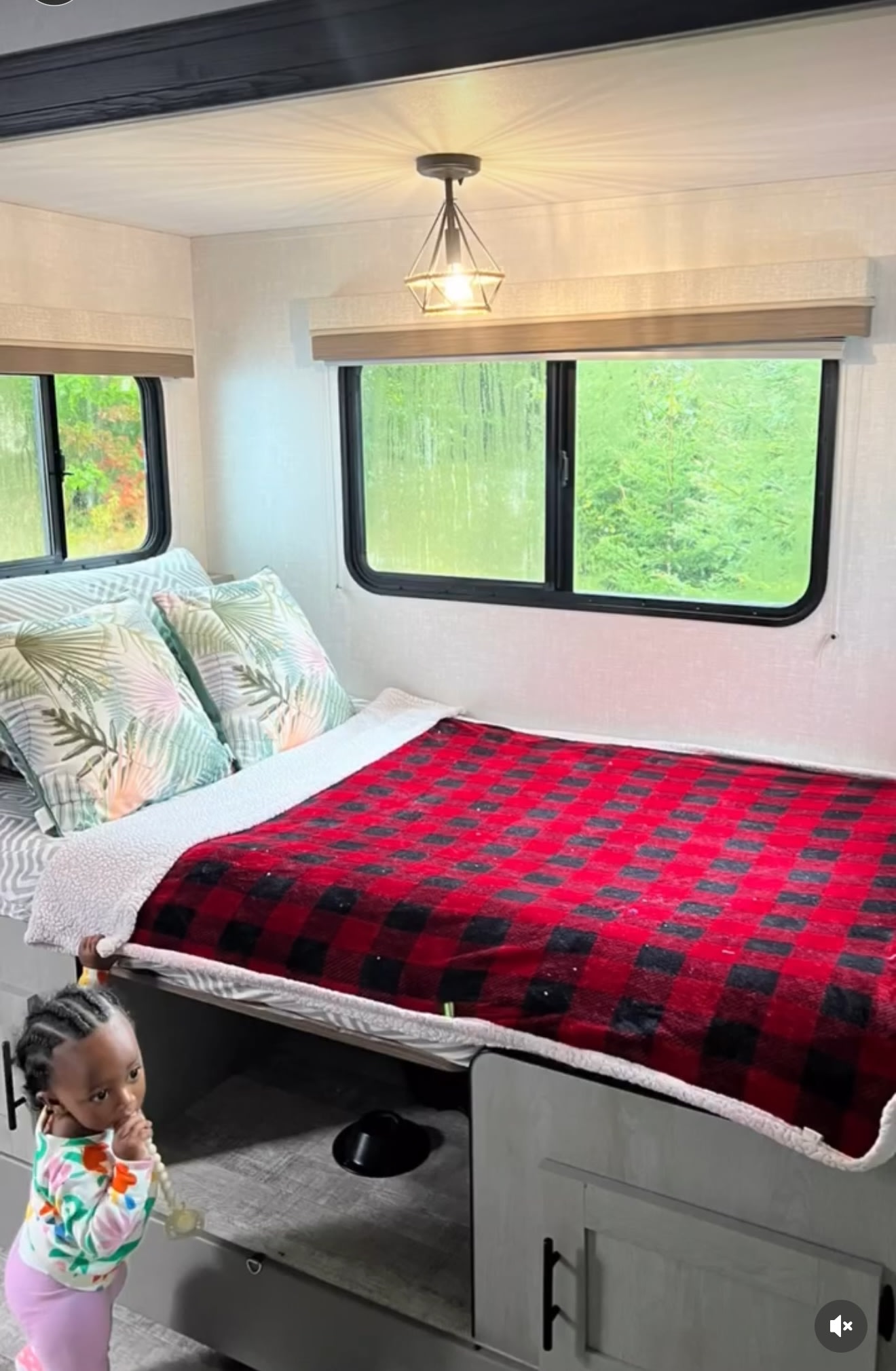 Inside a cozy RV rental bedroom: bed with plaid blanket, windows, & toddler playing. Ideal for travel.. Forest River IBEXMBS 2023
