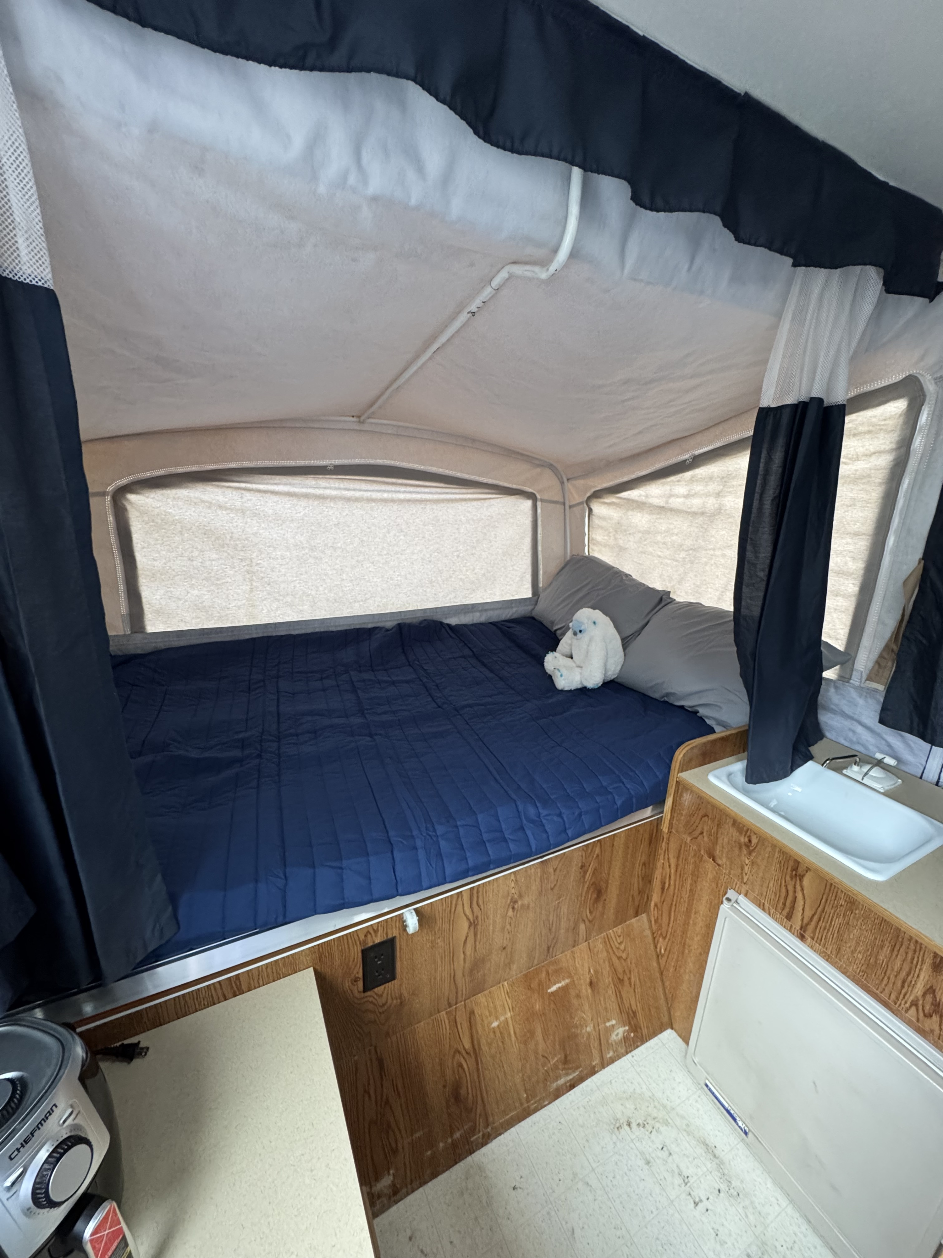 Inside an RV rental: a comfortable pop-up camper bed with blue bedding, a cute yeti, and a compact kitchen area.. Dutchmen Voyager 2000