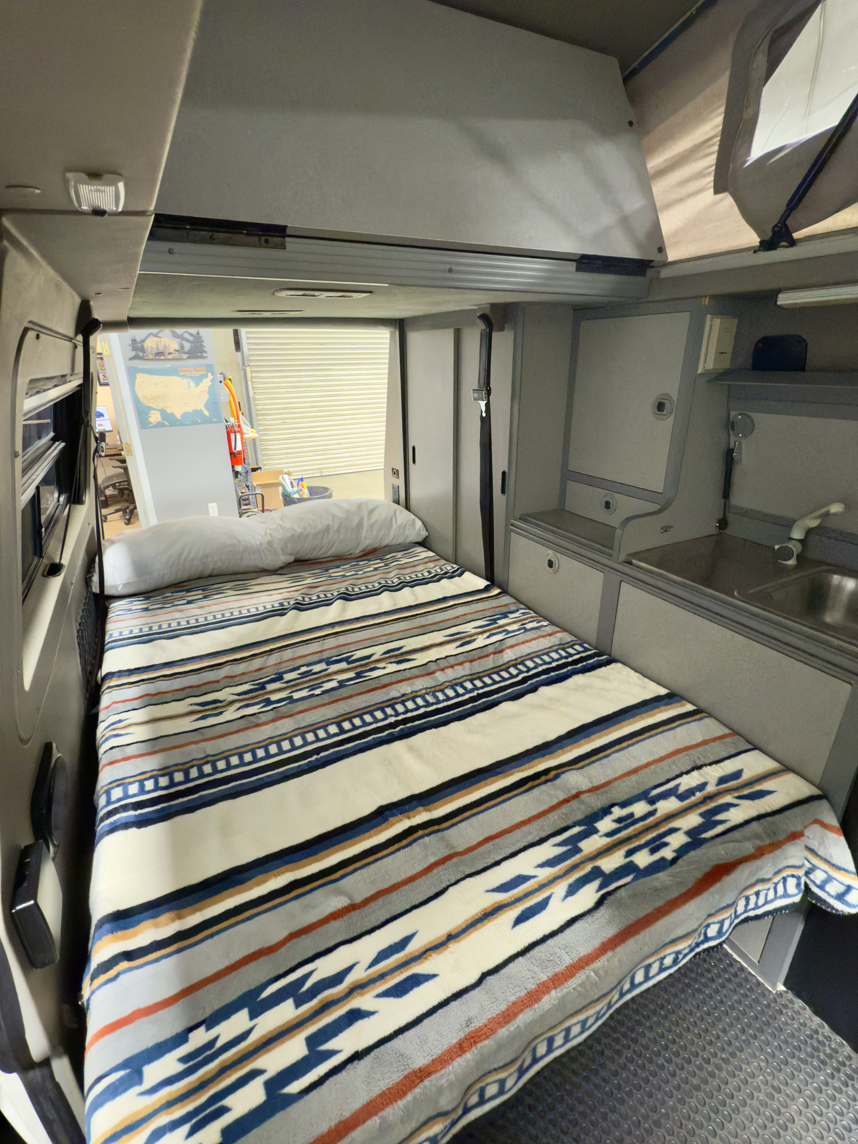 Cozy RV rental interior showcasing a patterned bed, compact kitchen with sink, and storage for adventures.. Winnebago Eurovan Camper Eurovan Camper 1999