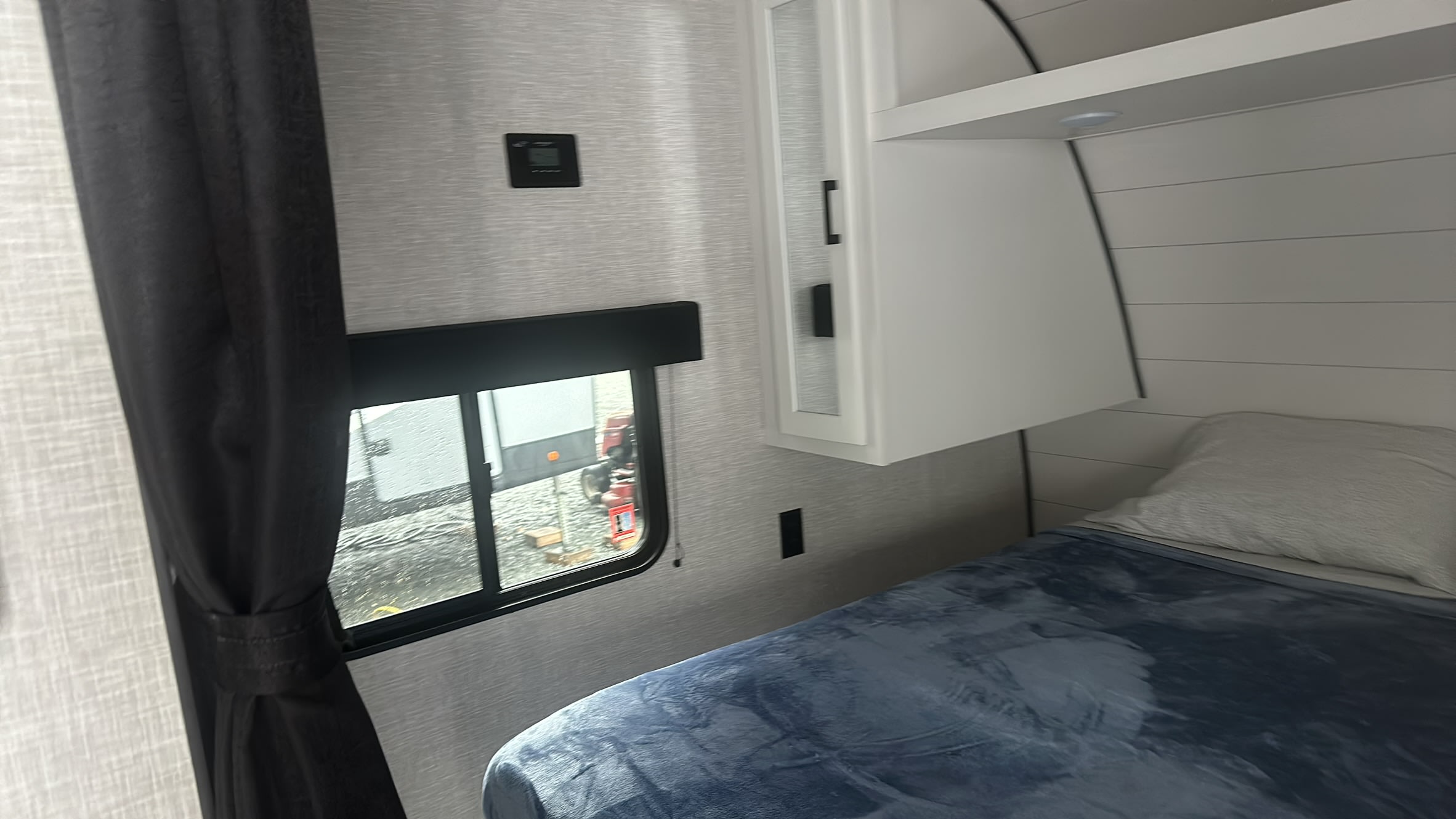 RV rental's cozy bedroom: blue bed, window, overhead cabinets, and thermostat. Perfect for mobile living.. Jayco Jay Flight 2024