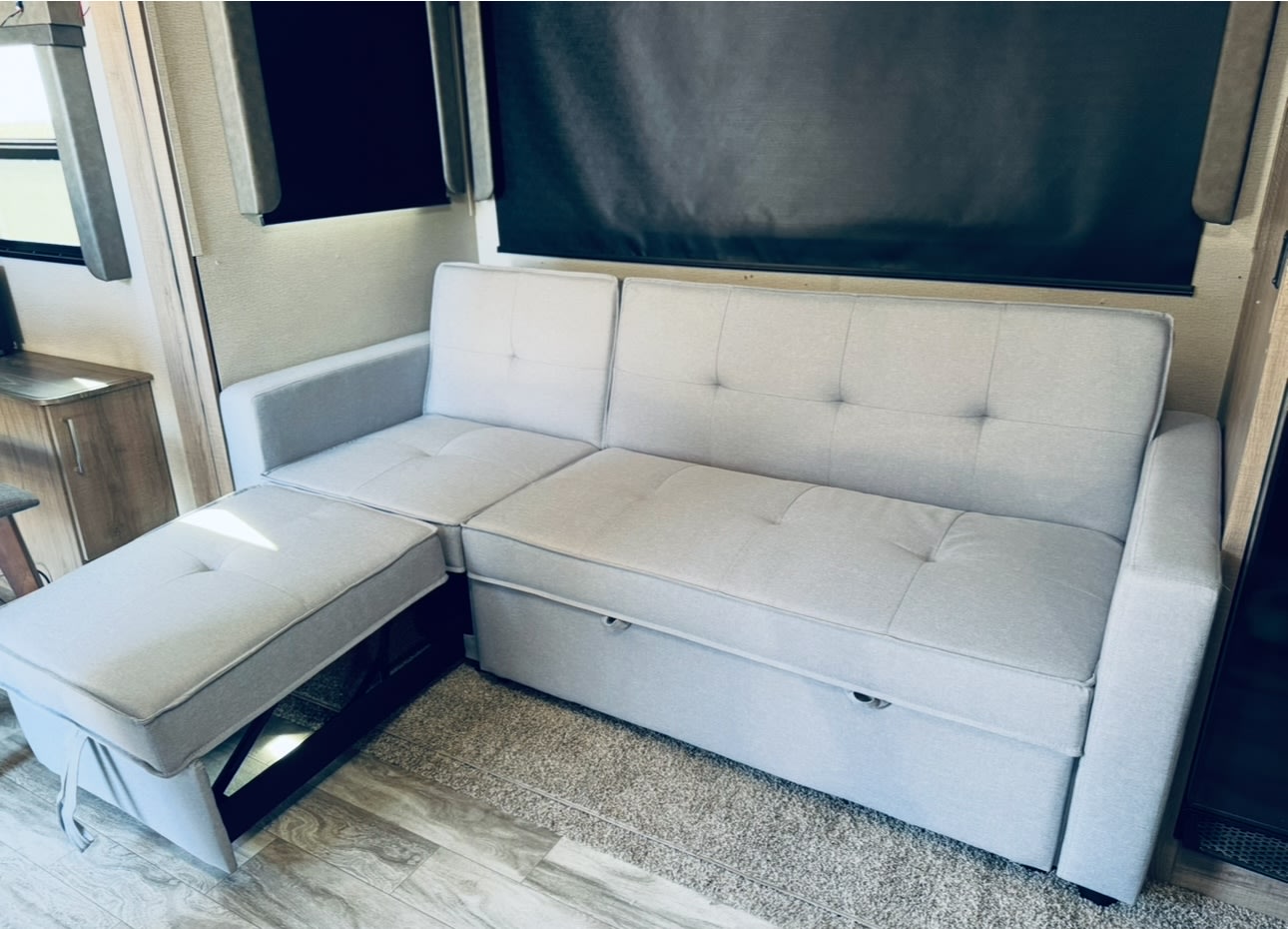 Light gray tufted sectional sofa, with an extending ottoman and hidden storage, offers comfort in this RV rental.. Grand Design Imagine 2022