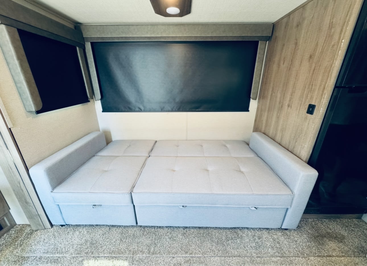 RV rental: Light gray convertible sofa bed with storage drawers, positioned under dark window blinds. Cozy interior for travel.. Grand Design Imagine 2022