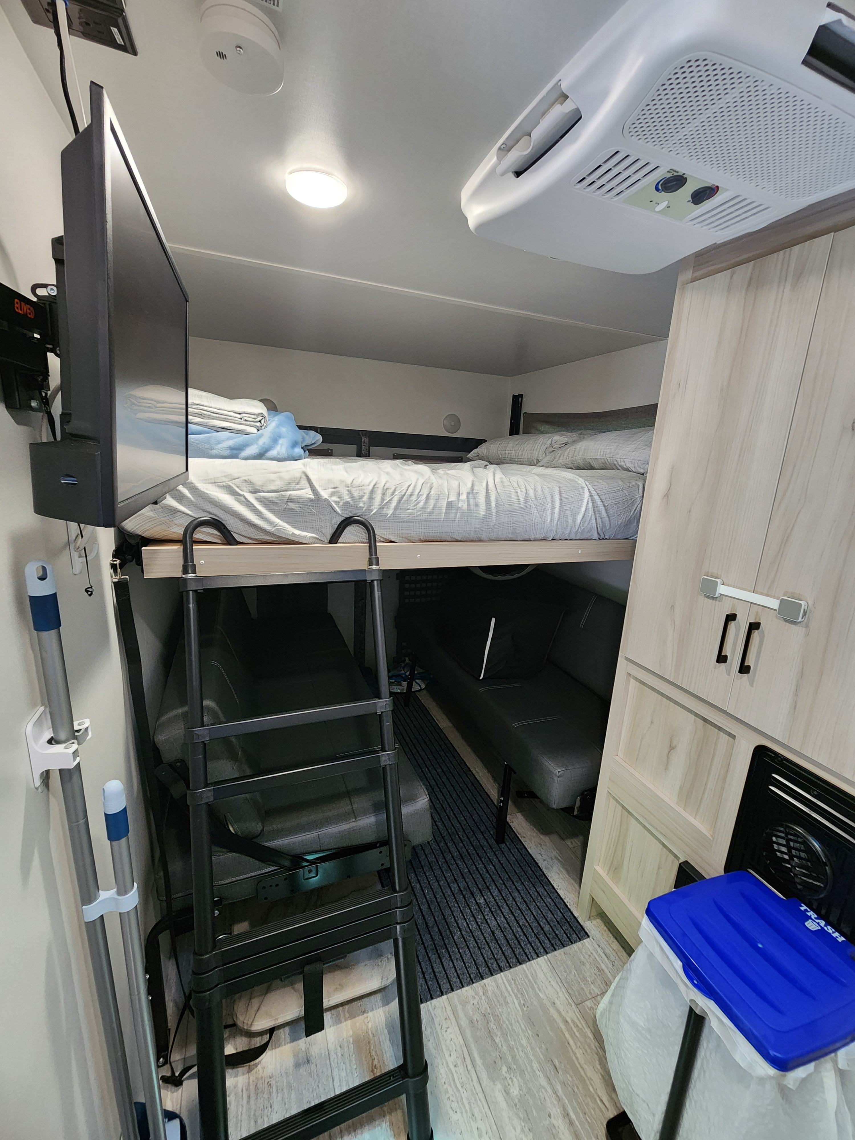 An RV rental's compact interior featuring bunk beds with a ladder, seating, and mounted TV.. Winnebago Other 2023