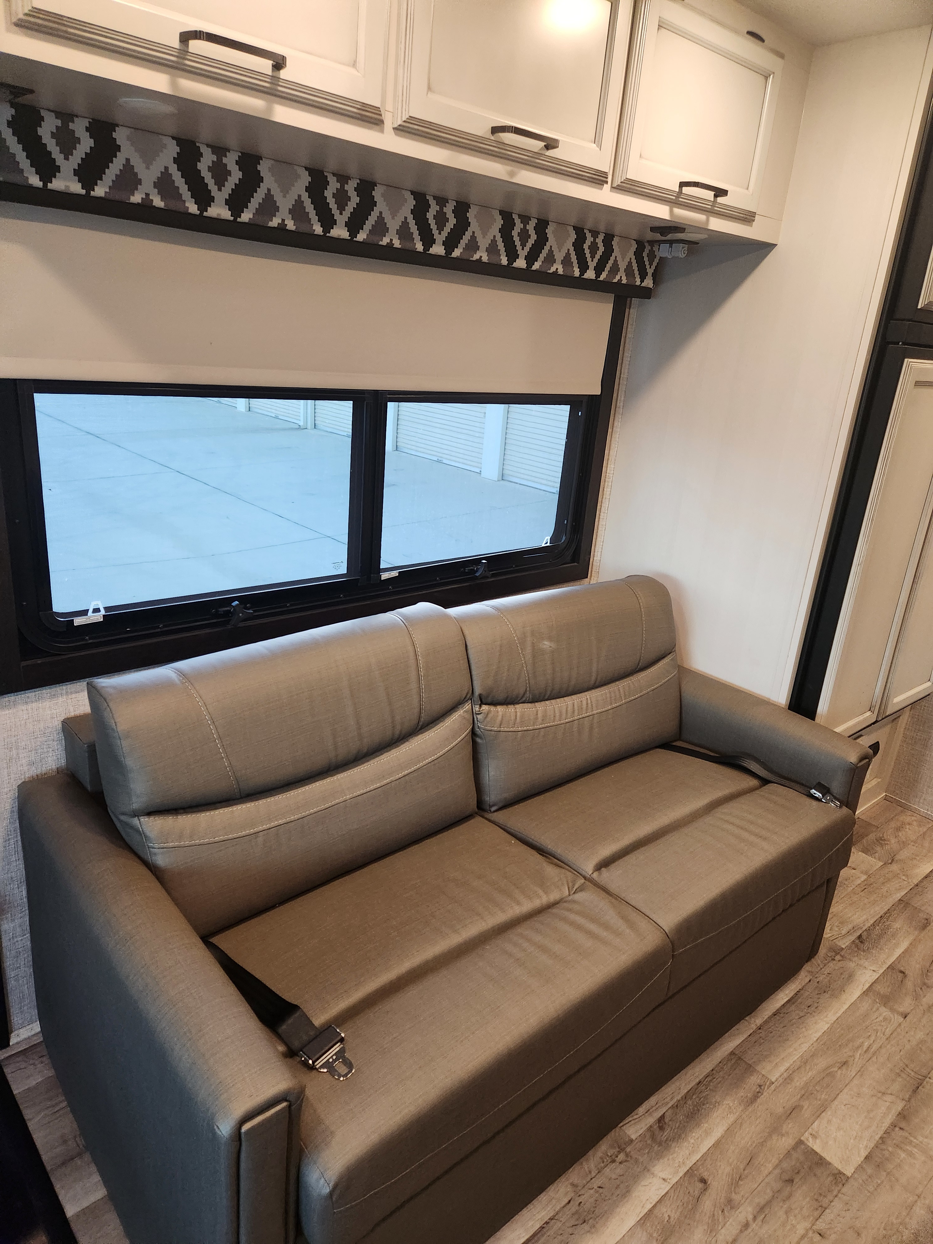 RV rental interior: Plush sofa with seatbelt, window with roller shade, and overhead storage cabinets.. Entegra Coach Vision 2022