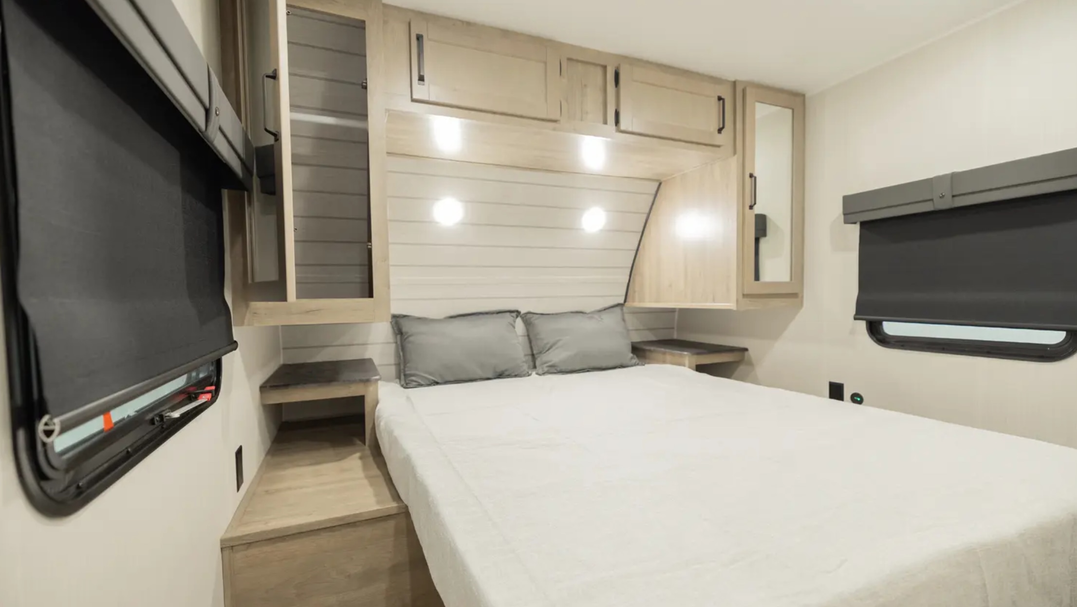 This RV rental bedroom features a comfortable bed, overhead cabinets, and dark roller blinds on the windows, offering a cozy space.. Palomino Puma 2024