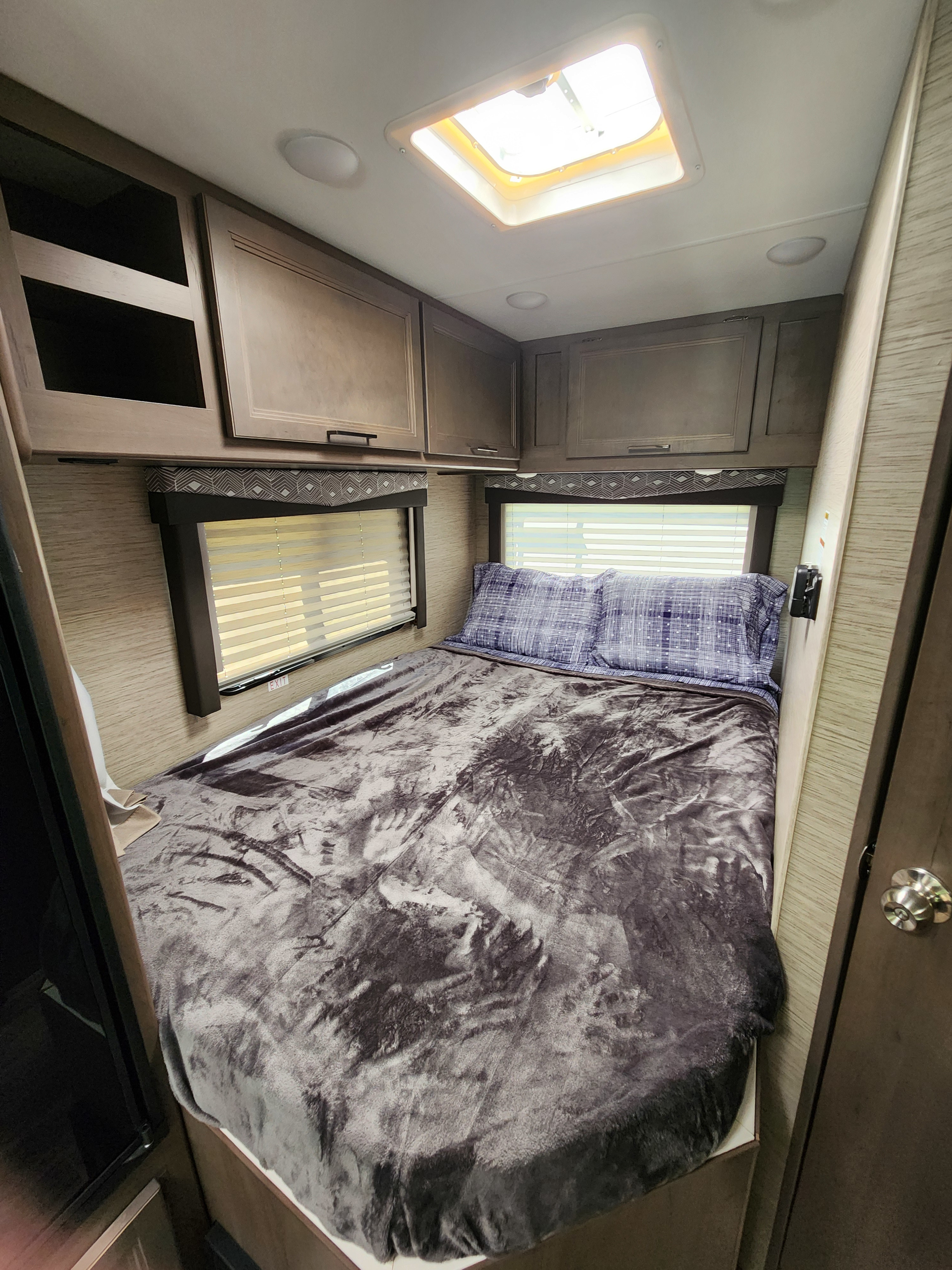 RV rental bedroom: a cozy interior with bed, patterned pillows, windows, overhead cabinets, and a bright ceiling skylight.. Thor Motor Coach Four Winds 2023