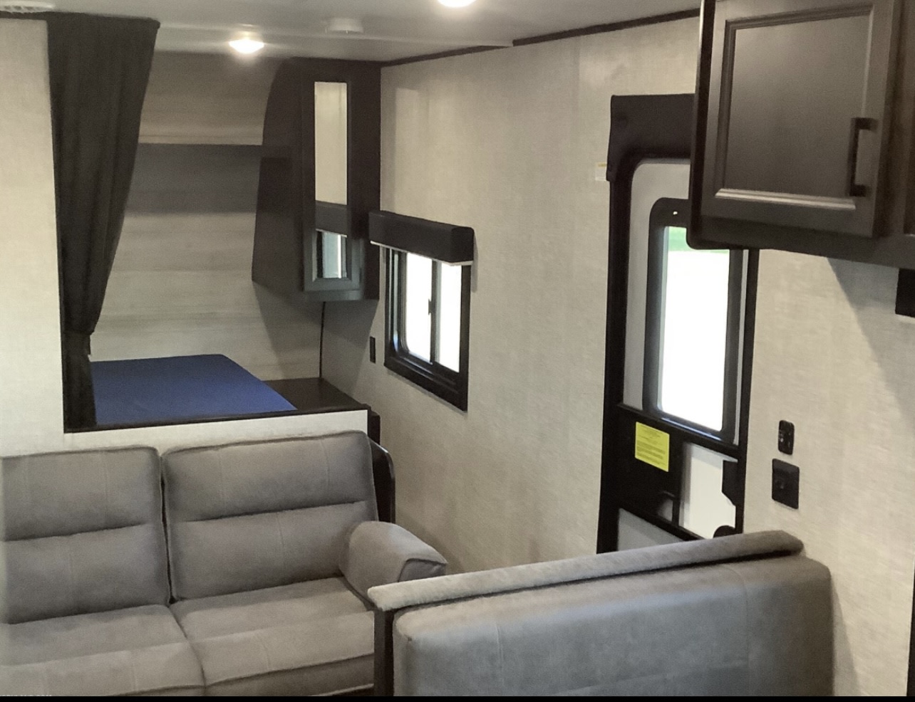 Compact RV rental interior: living space with gray sofa, adjacent bedroom, main door, & windows for natural light.. Jayco Jay Flight SLX Rocky Mountain Edition 2022