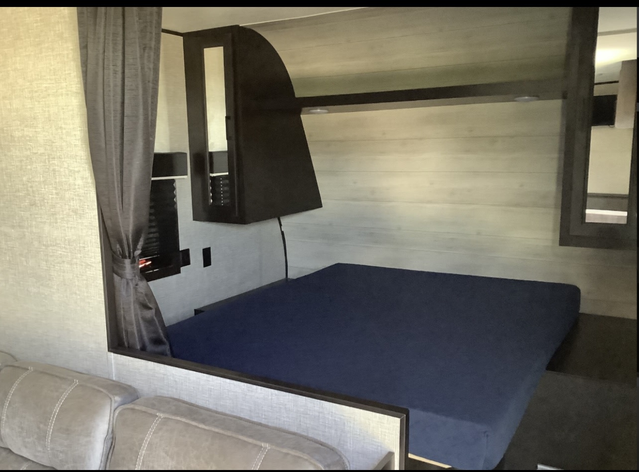 RV rental interior: View of a compact bedroom with a navy mattress, overhead storage, and a tied-back privacy curtain.. Jayco Jay Flight SLX Rocky Mountain Edition 2022