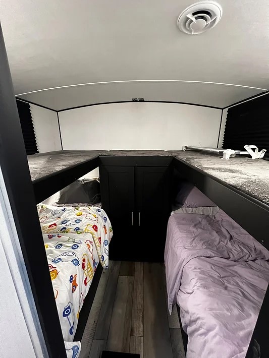 Interior of an **rv rental** bunk room: two lower beds with upper sleeping platforms and a central storage cabinet.. Keystone RV Springdale 2023