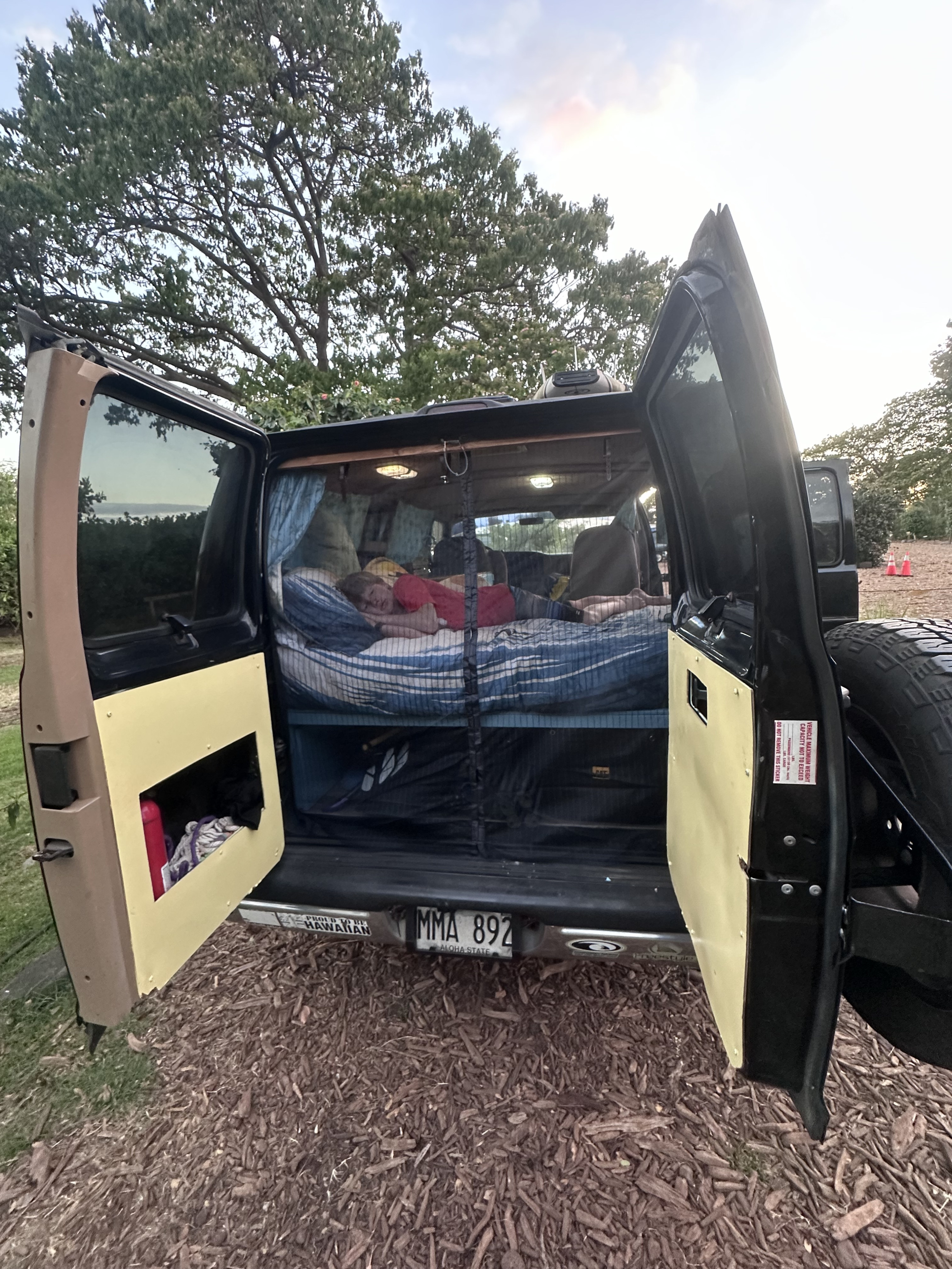 An RV rental camper van with open back doors. A person sleeps on a bed inside, a Hawaii license plate visible.. Dodge 1500 1999