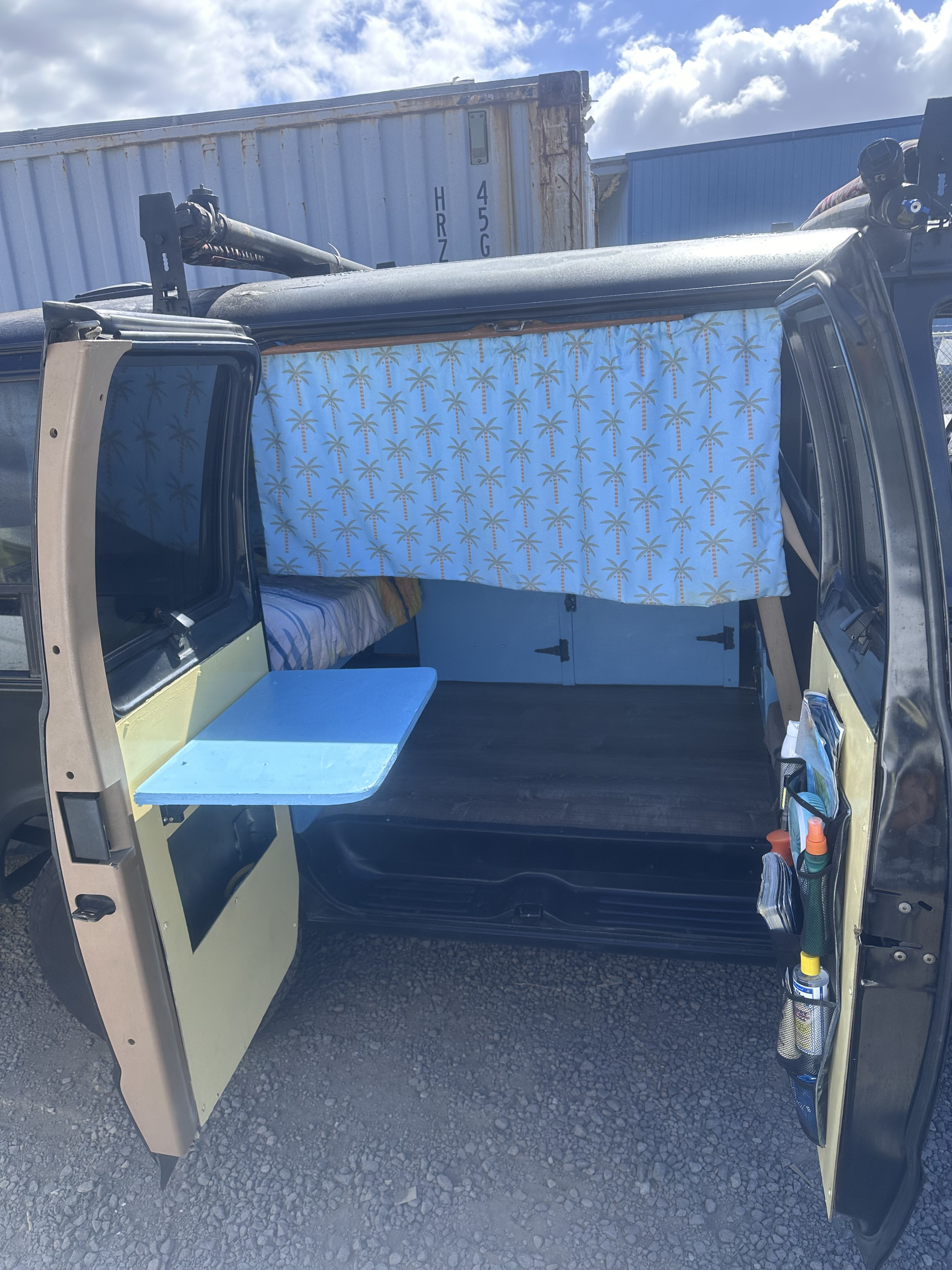This rv rental features a custom camper van interior: blue palm tree curtain, bed, and a handy fold-down table.. Dodge 1500 1999