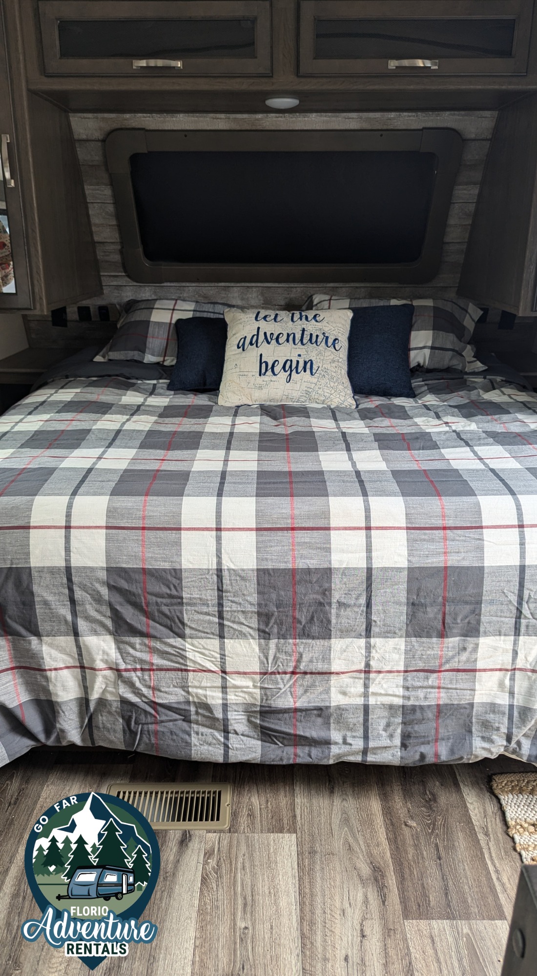 Cozy RV rental bedroom featuring a large bed with grey, white, and red plaid bedding, and an "adventure" pillow.. Keystone RV Cougar 2021