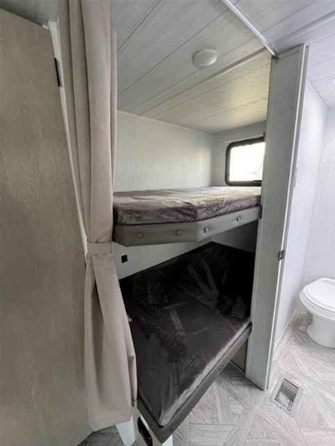Inside an RV rental, featuring stacked bunk beds with privacy curtains and a compact adjacent bathroom setup.. Forest River Salem 2024