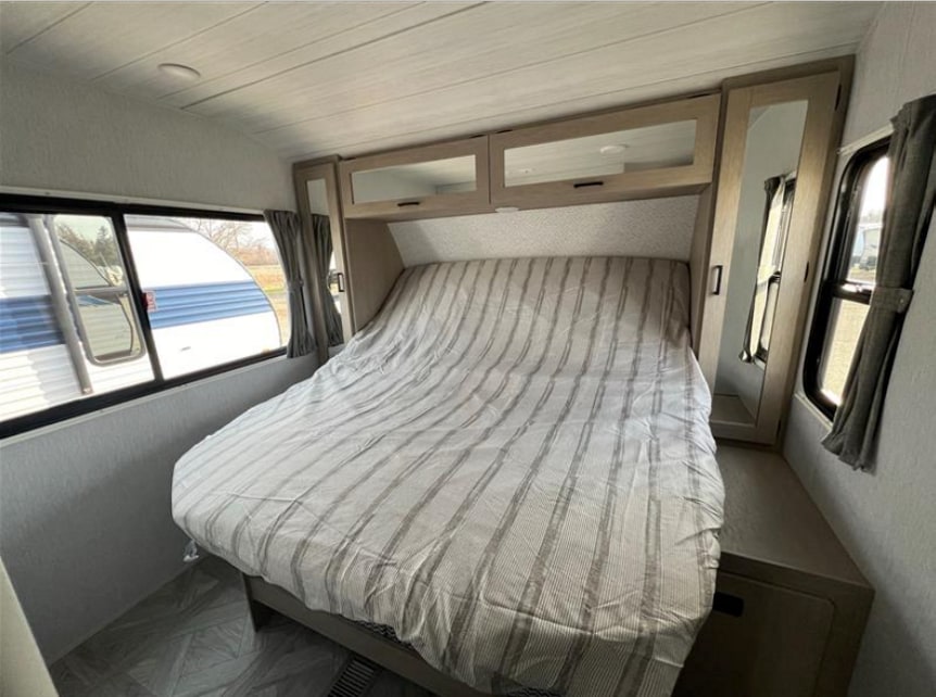 RV rental bedroom with a large, striped bed, overhead storage, and mirrored cabinet. Windows offer exterior views.. Forest River Salem 2024