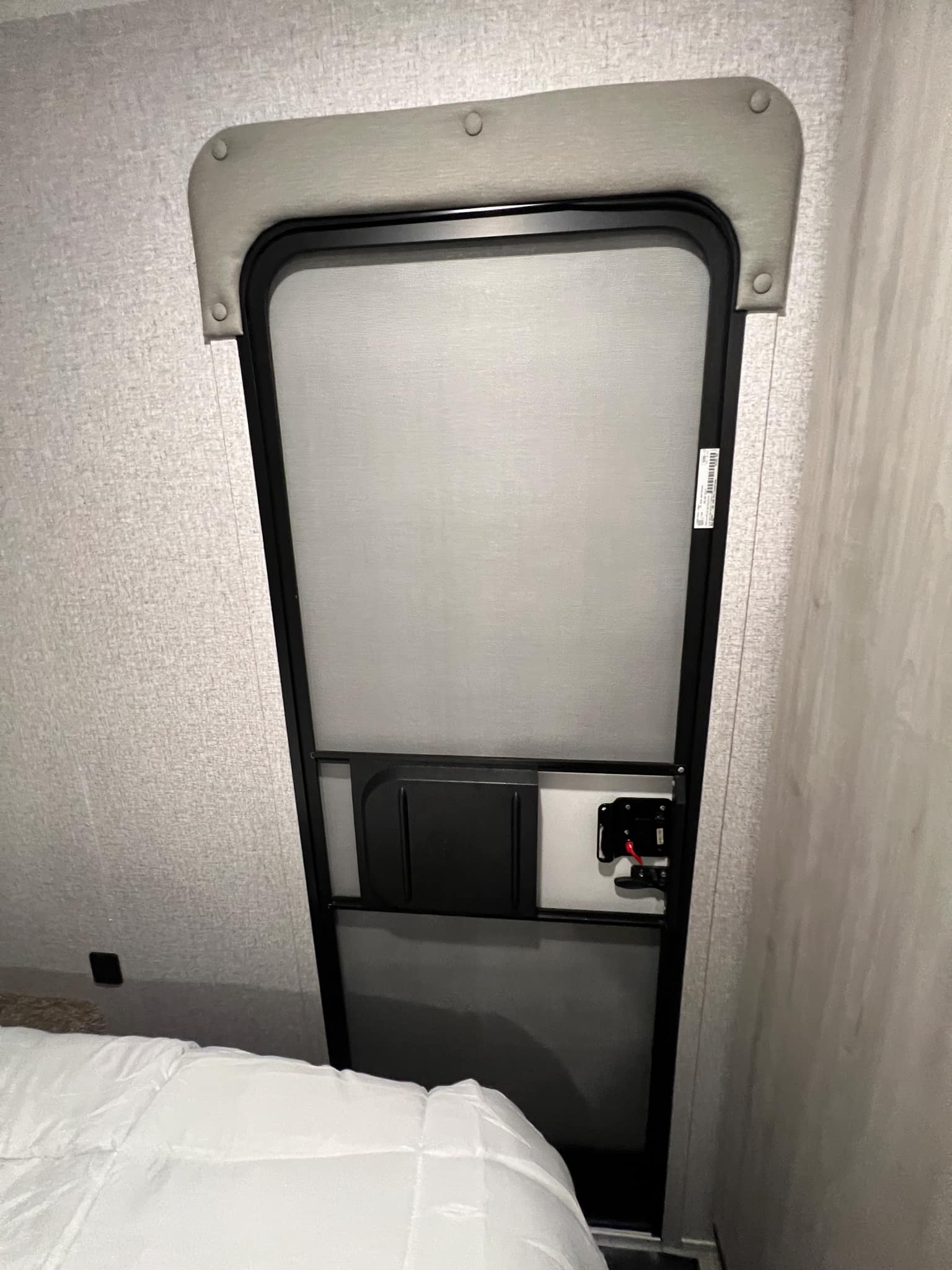 RV rental interior: A closed RV screen door with a pulled-down sunshade, fabric valance, and part of a bed.. East to West Silver Lake 2022
