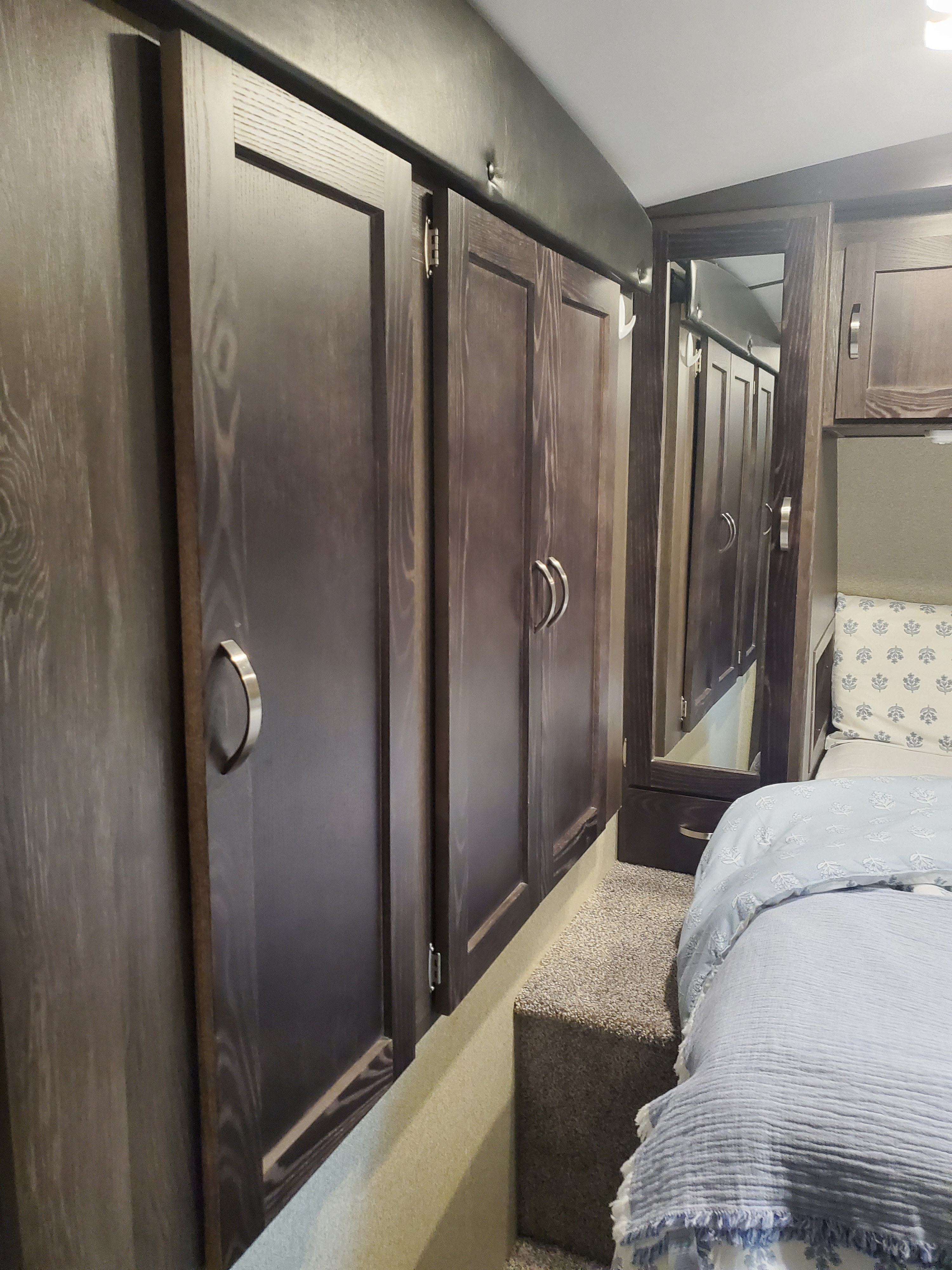 Spacious RV rental bedroom featuring dark wood cabinets, a full-length mirror, and a cozy bed with light blue linens.. Keystone Outback 2018