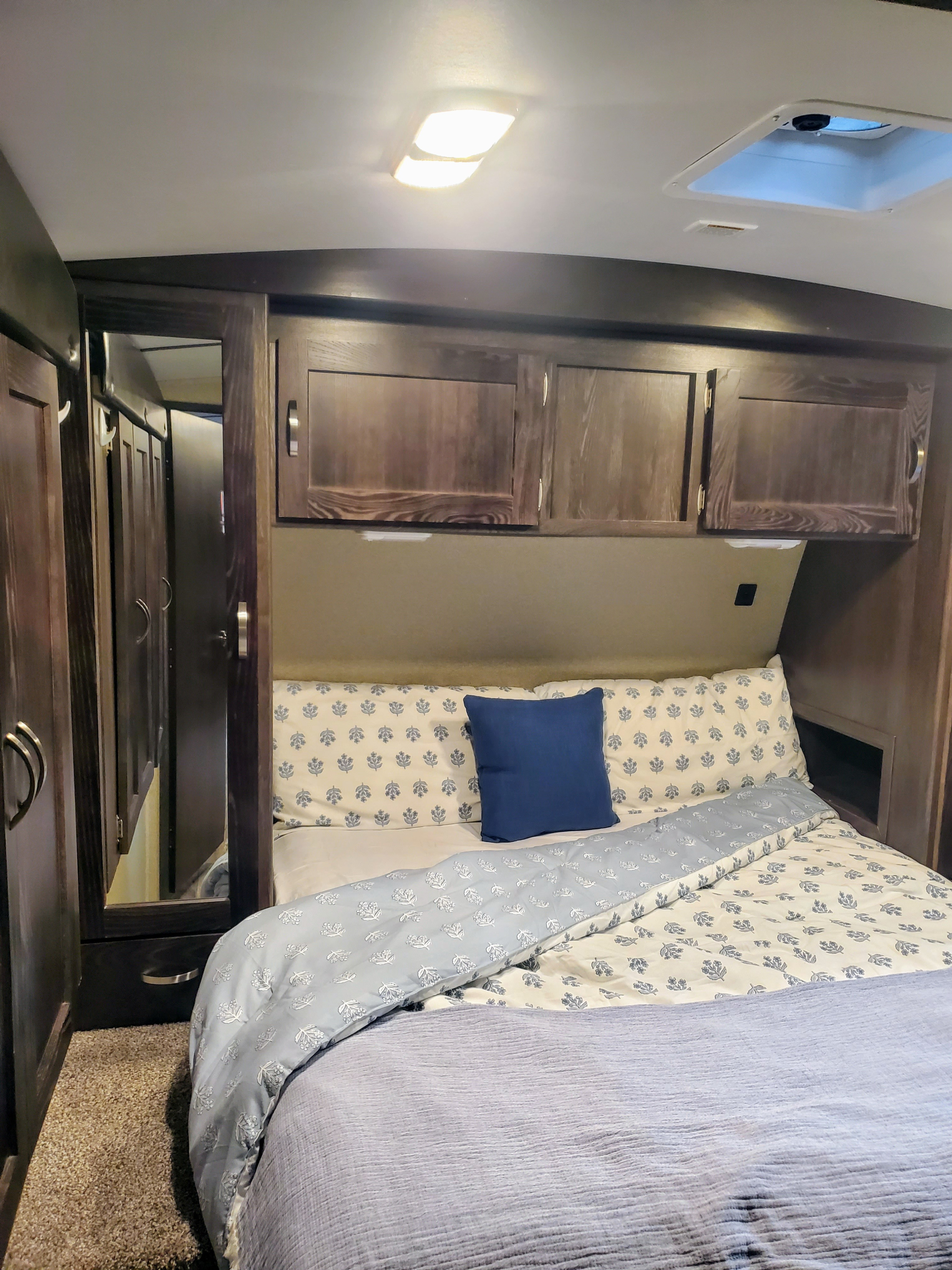 Cozy RV rental bedroom with patterned bedding, overhead storage, wardrobe, and ceiling light. Ideal for travel.. Keystone Outback 2018