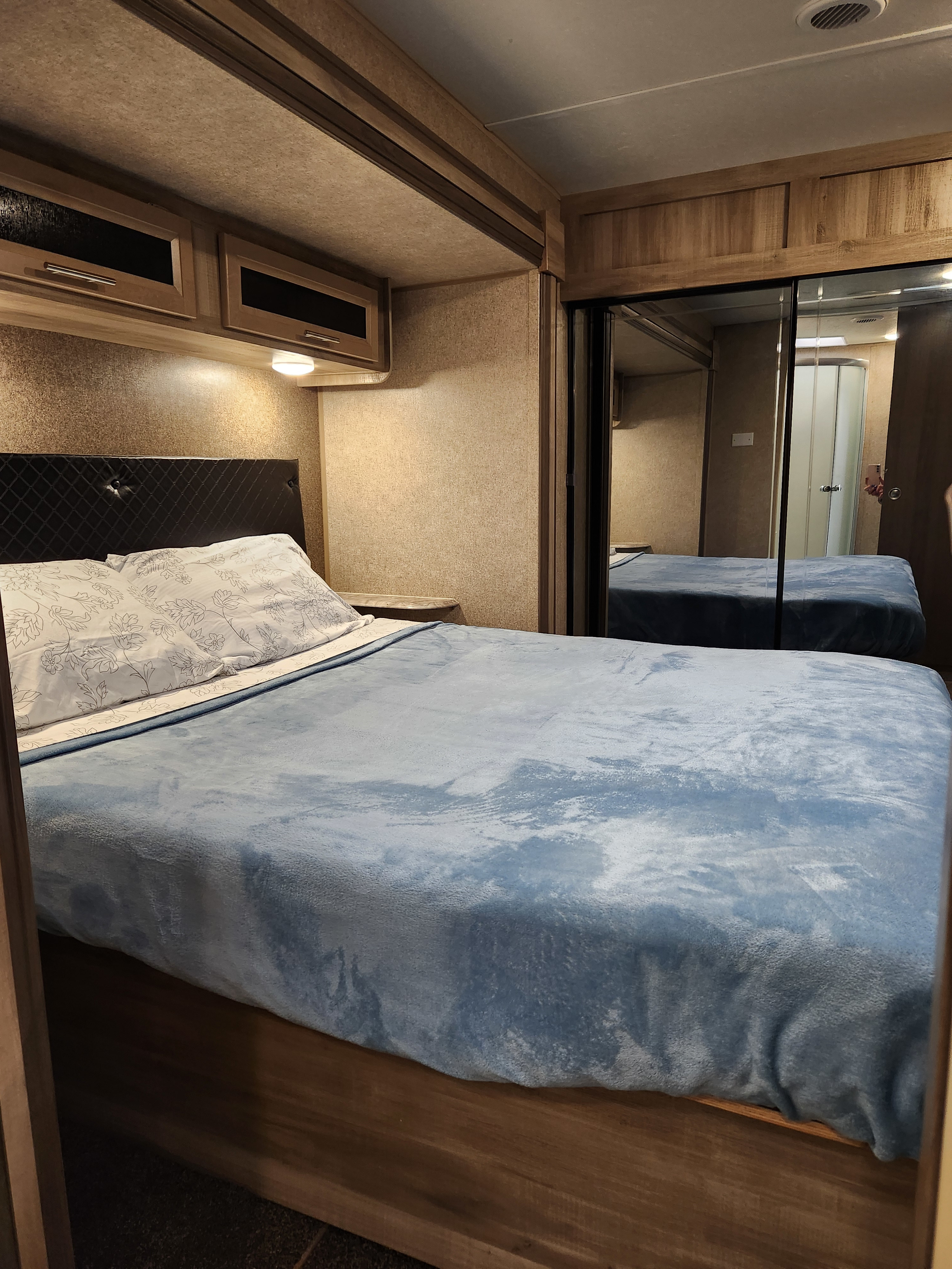 Cozy RV rental bedroom features a comfortable bed with blue blanket, overhead storage, and mirrored closet. Ready for adventure!. Coachmen Catalina 2020