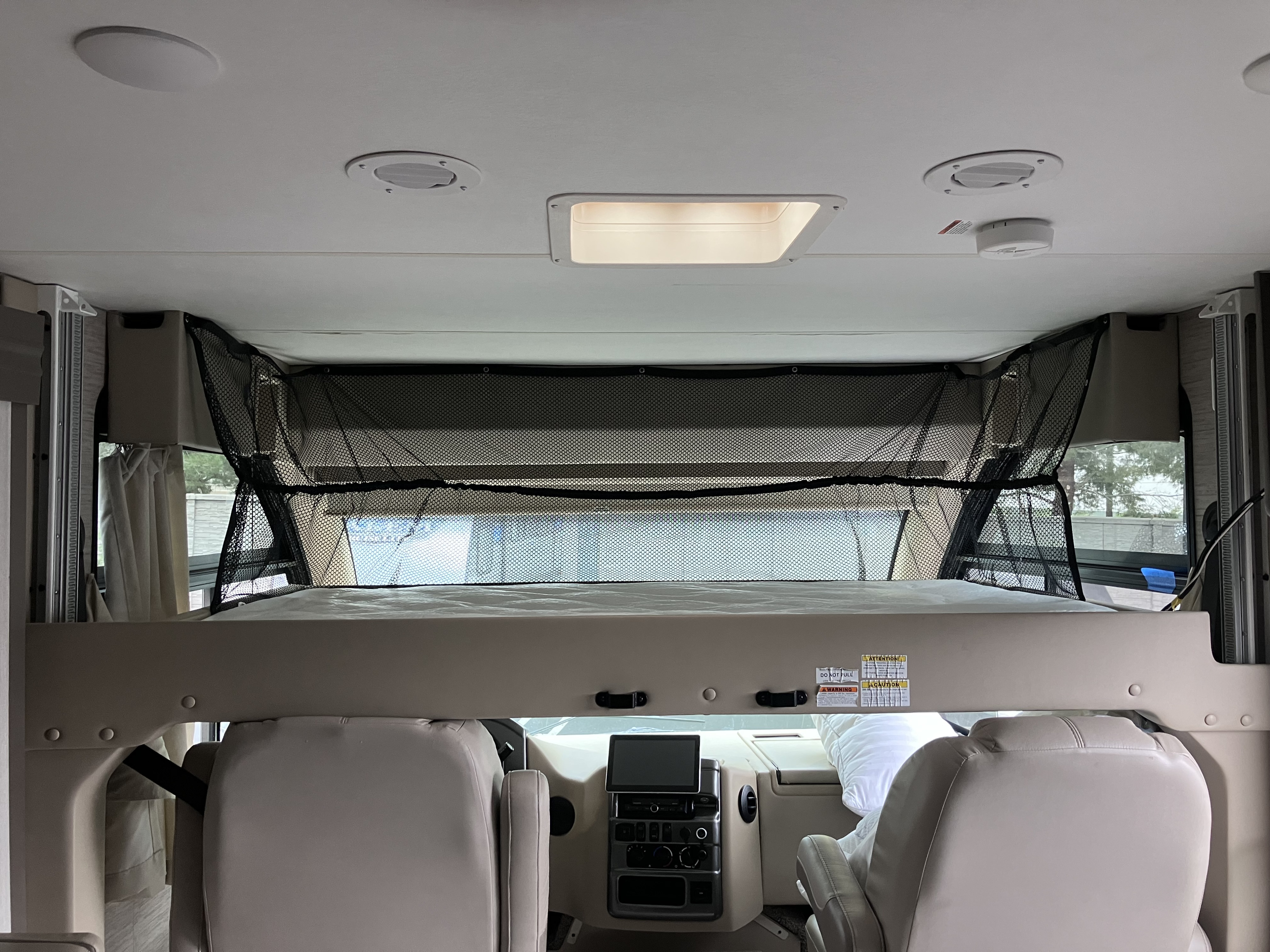 This RV rental shows an overhead bunk bed with a safety net above the driver's cabin, featuring the dashboard and front seats.. Thor Motor Coach Vegas 2022