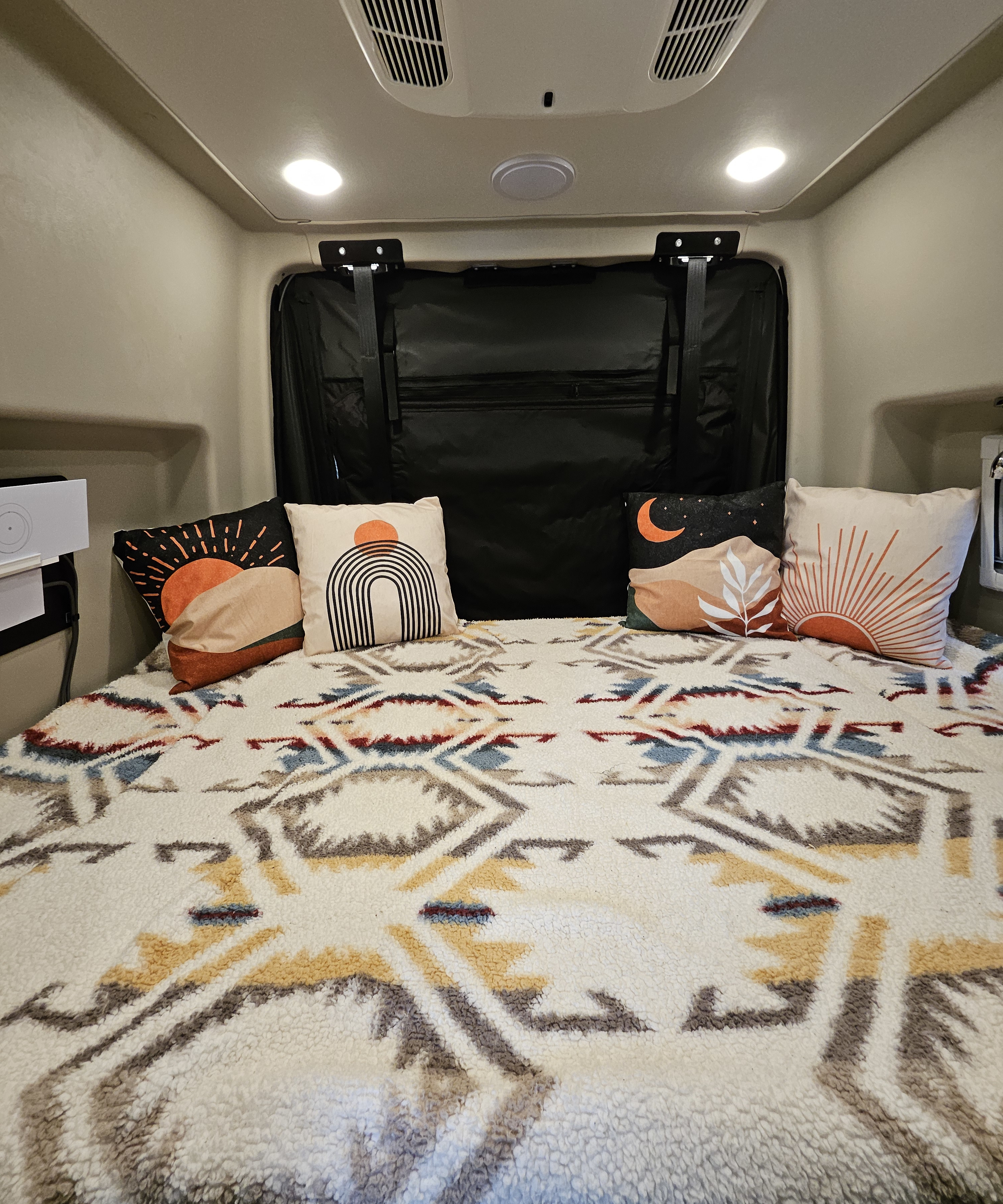 Comfortable RV rental bed with stylish desert-themed pillows & a warm, textured geometric blanket for cozy travels.. Entegra Coach Launch 2023