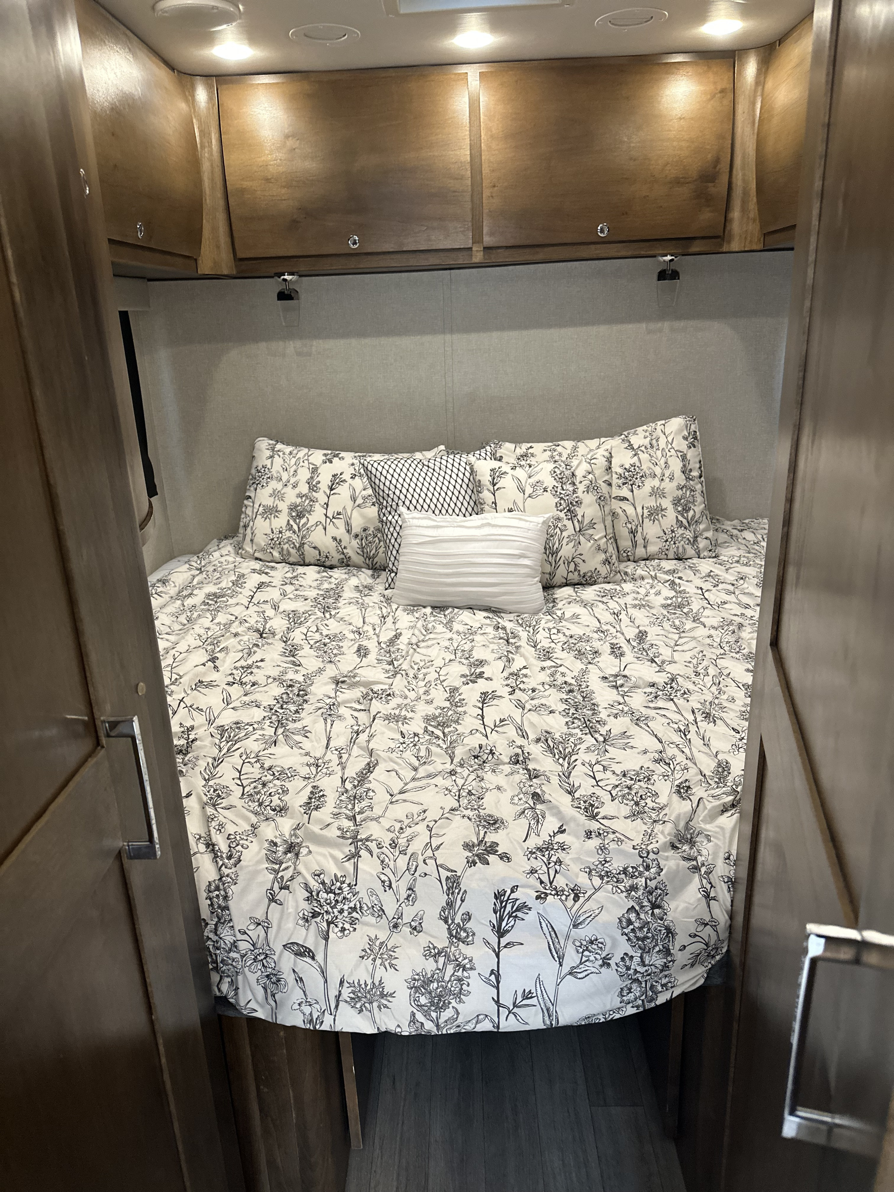 Step into this comfortable rv rental bedroom, featuring floral bedding, spacious overhead cabinets, and soft lighting.. Wayfarer Wayfarer Motorhome 2018