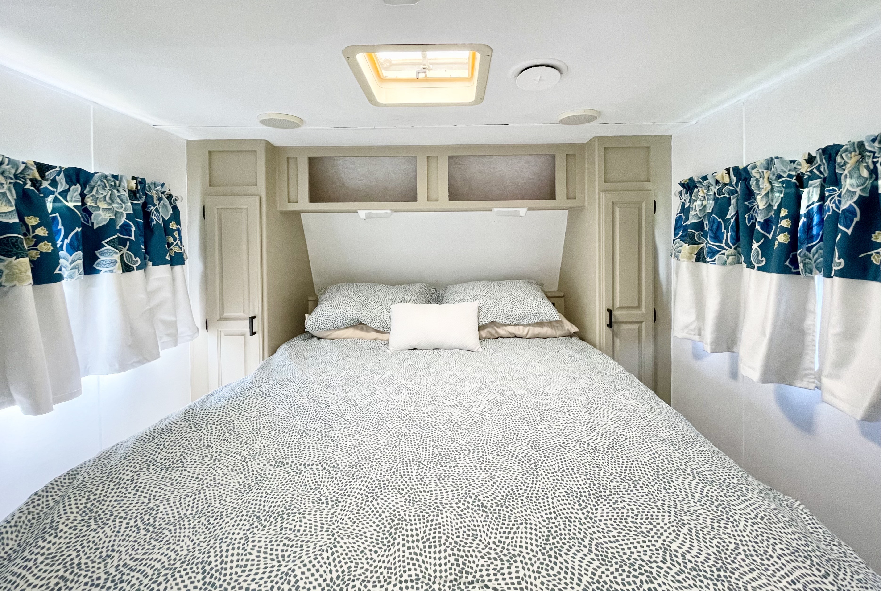 Enjoy a cozy RV rental bedroom. Features include patterned bedding, blue floral valance curtains, and ample overhead storage.. Jayco Eagle 1998