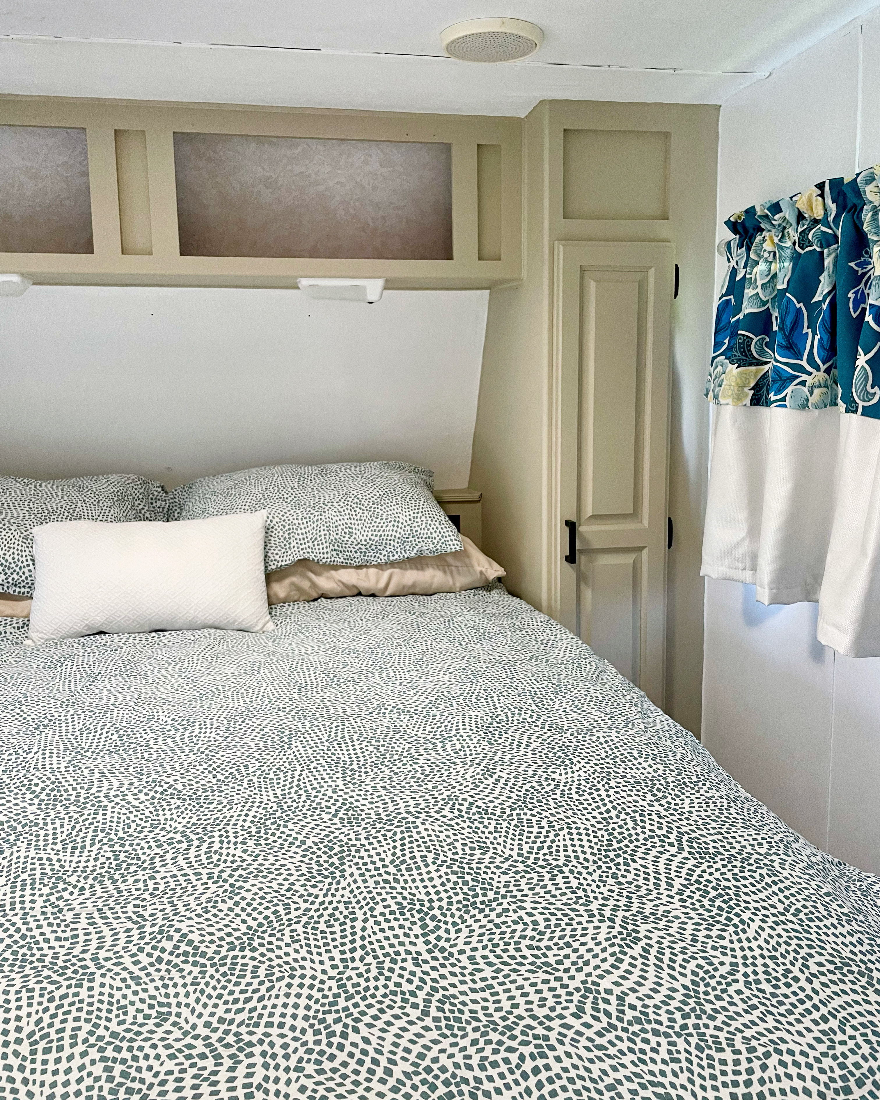 Cozy RV rental bedroom featuring patterned bedding, overhead cabinets, and bright floral curtains for a comfy stay.. Jayco Eagle 1998