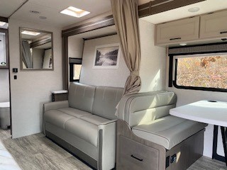 This RV rental interior offers a comfy sofa bed, dinette, and bright windows, ideal for travel and camping adventures.. Thor Magnitude GA 2024