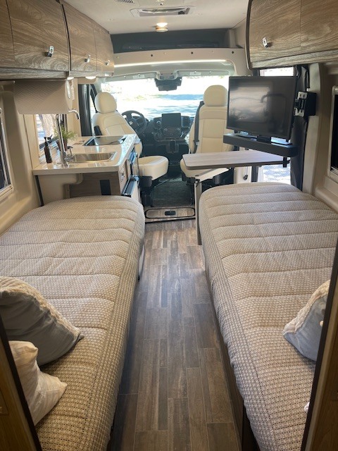 Clean rv rental interior featuring two comfortable beds, a kitchenette, and forward cockpit views.. Winnebago Travato 2023