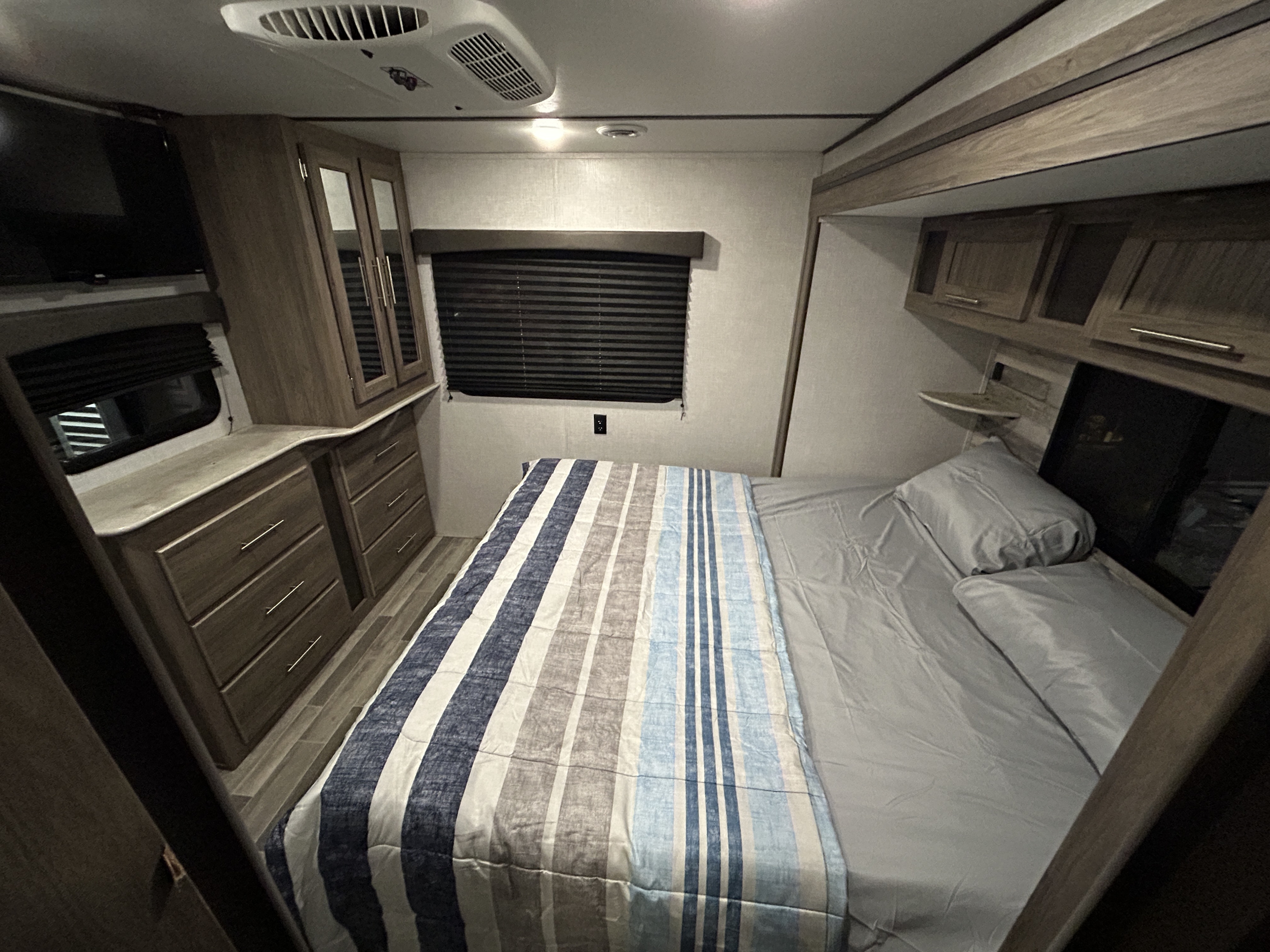 Cozy RV rental bedroom interior: a comfortable bed with striped comforter, TV, and ample storage for your camper getaway.. Crossroads Zinger 2021