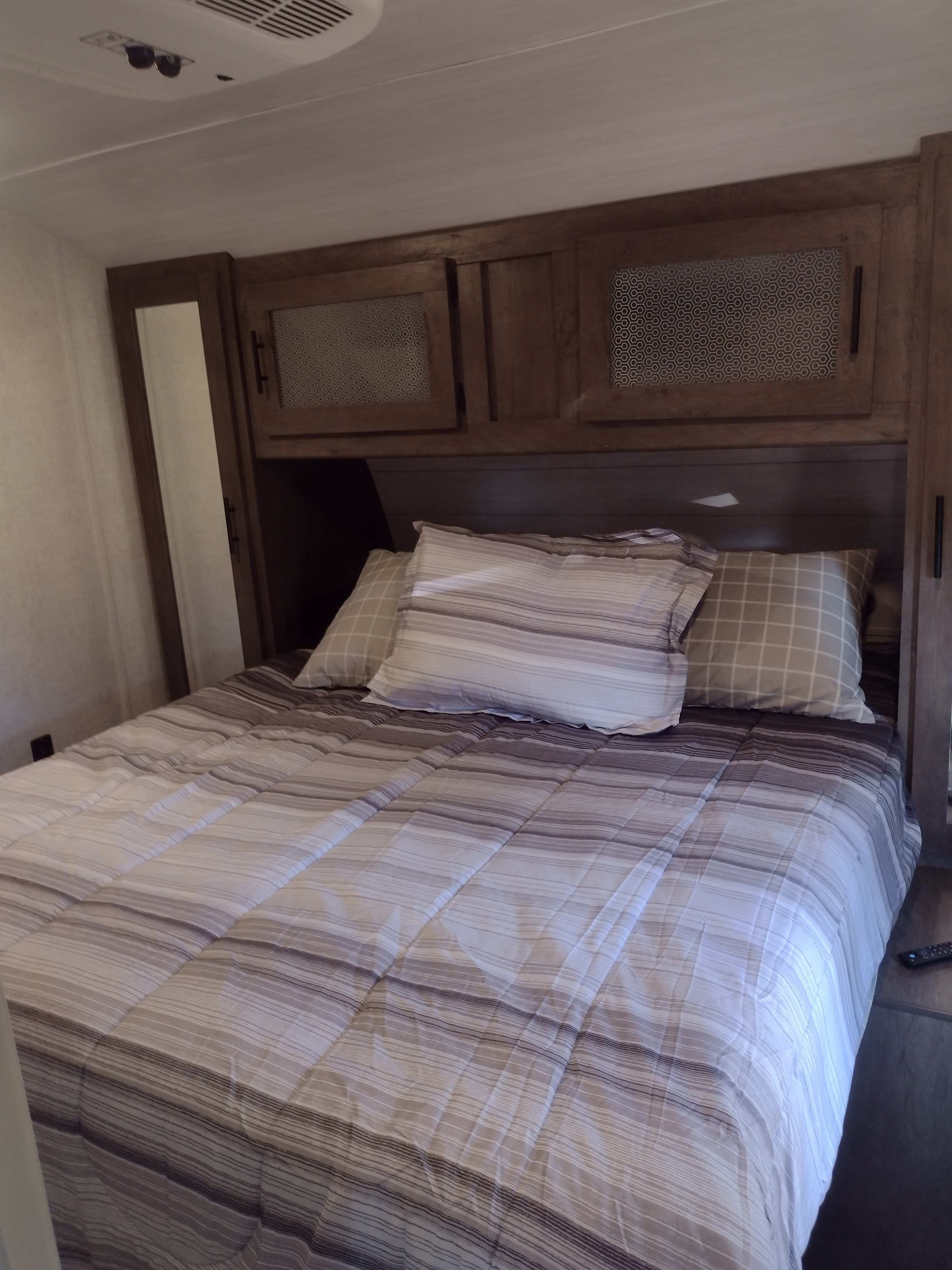 RV rental bedroom: striped bedding, plaid pillows, wood cabinets, and ceiling AC unit for comfort.. Forest River Wildwood 2021