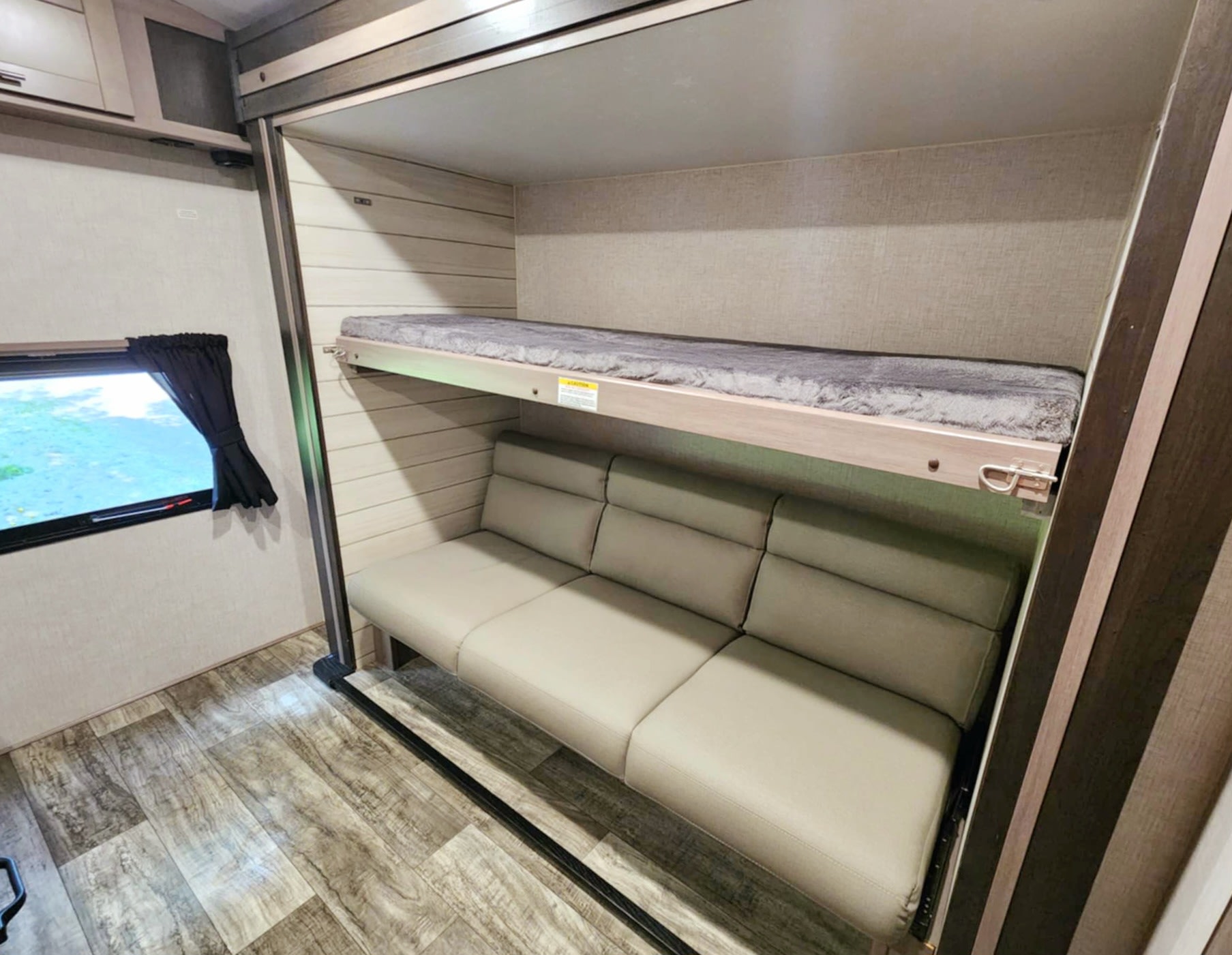 Compact RV rental interior: bunk beds with a soft mattress above a beige sofa, set against paneling and wood-look flooring.. Crossroads RV Sunset Trail 2022