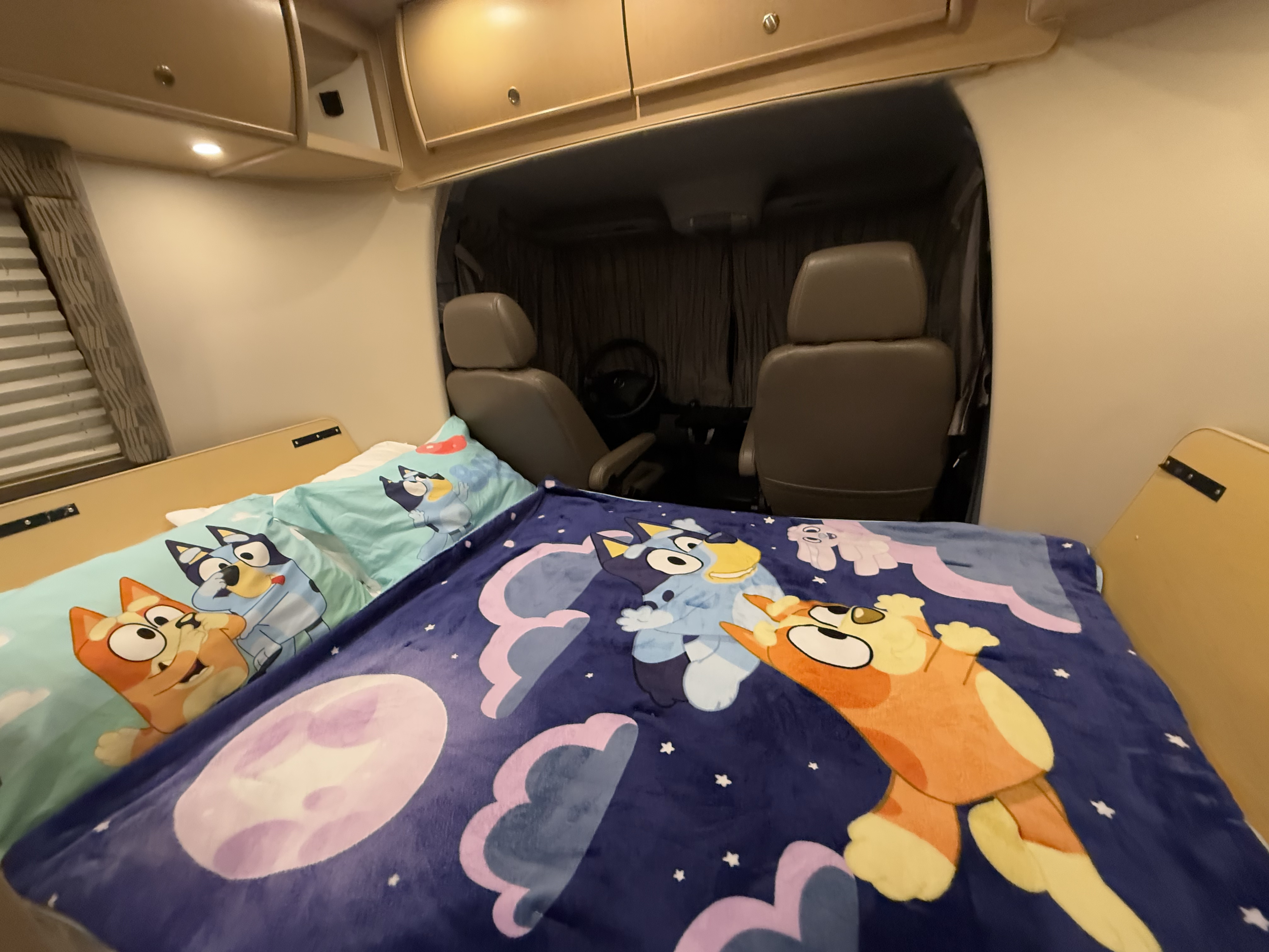 Cozy RV rental bed with Bluey-themed bedding, overlooking the driver's cabin. Perfect for family adventures.. Leisure Travel Vans Serenity 2013