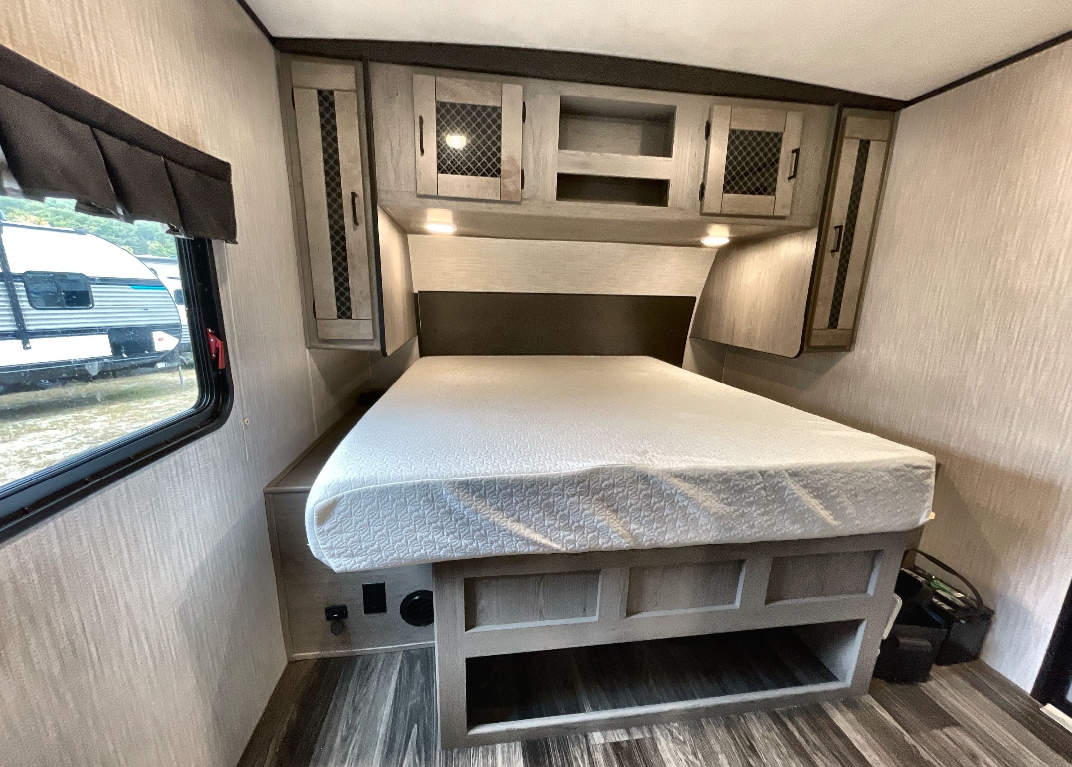 This RV rental bedroom features a white mattress on a bed frame with storage, overhead cabinets, and a window.. Heartland Mallard 2021
