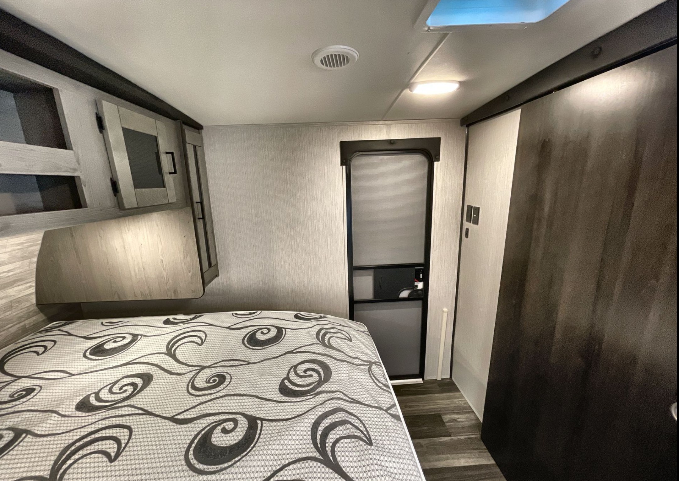 Discover this cozy rv rental bedroom: patterned bed, overhead storage, and a private door. Your comfortable travel awaits!. Heartland Mallard 2021