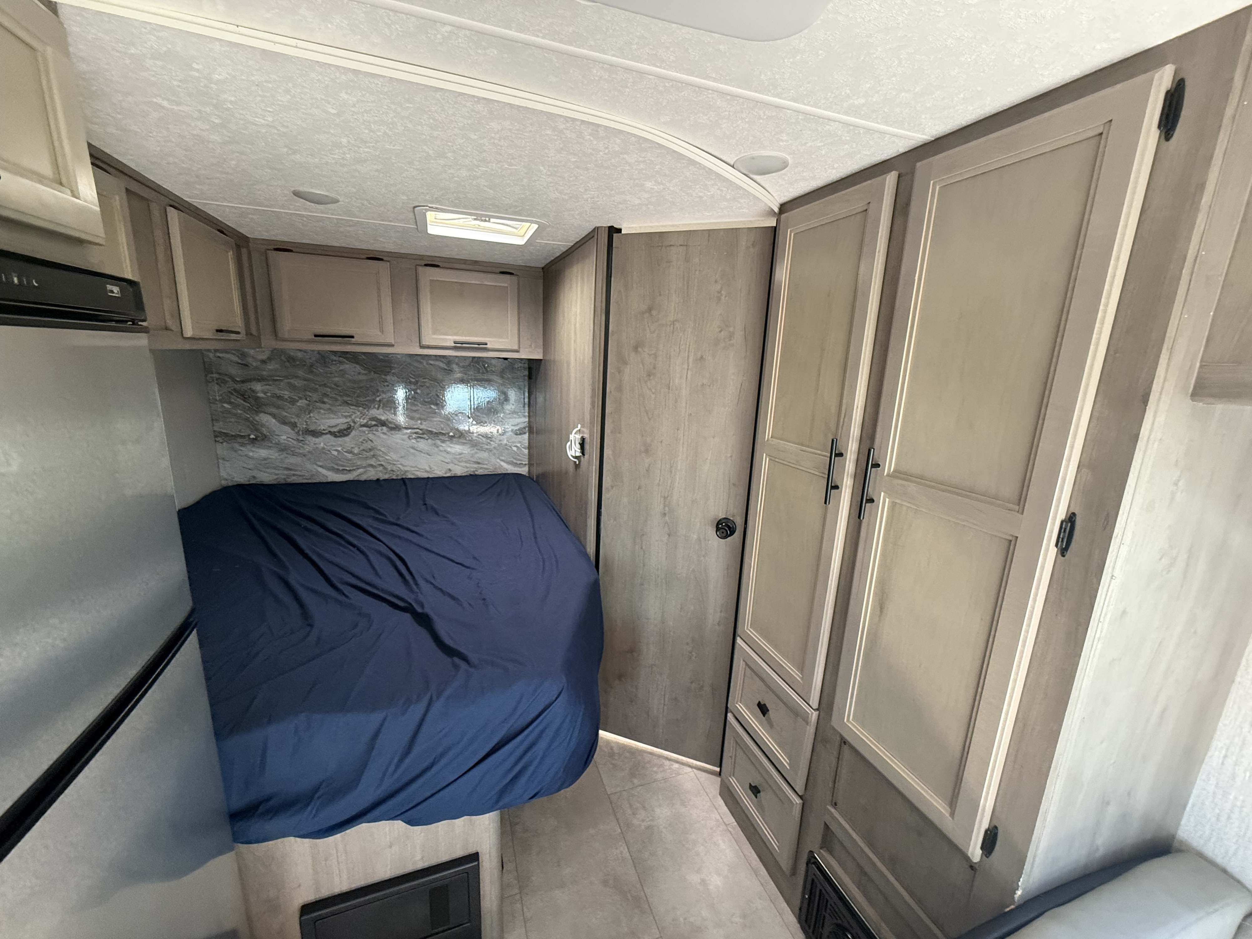 Inside this RV rental: a compact living space with a comfortable bed, overhead cabinets, and a refrigerator.. 1HAGGUC78MN008793 Cross Trail 2022