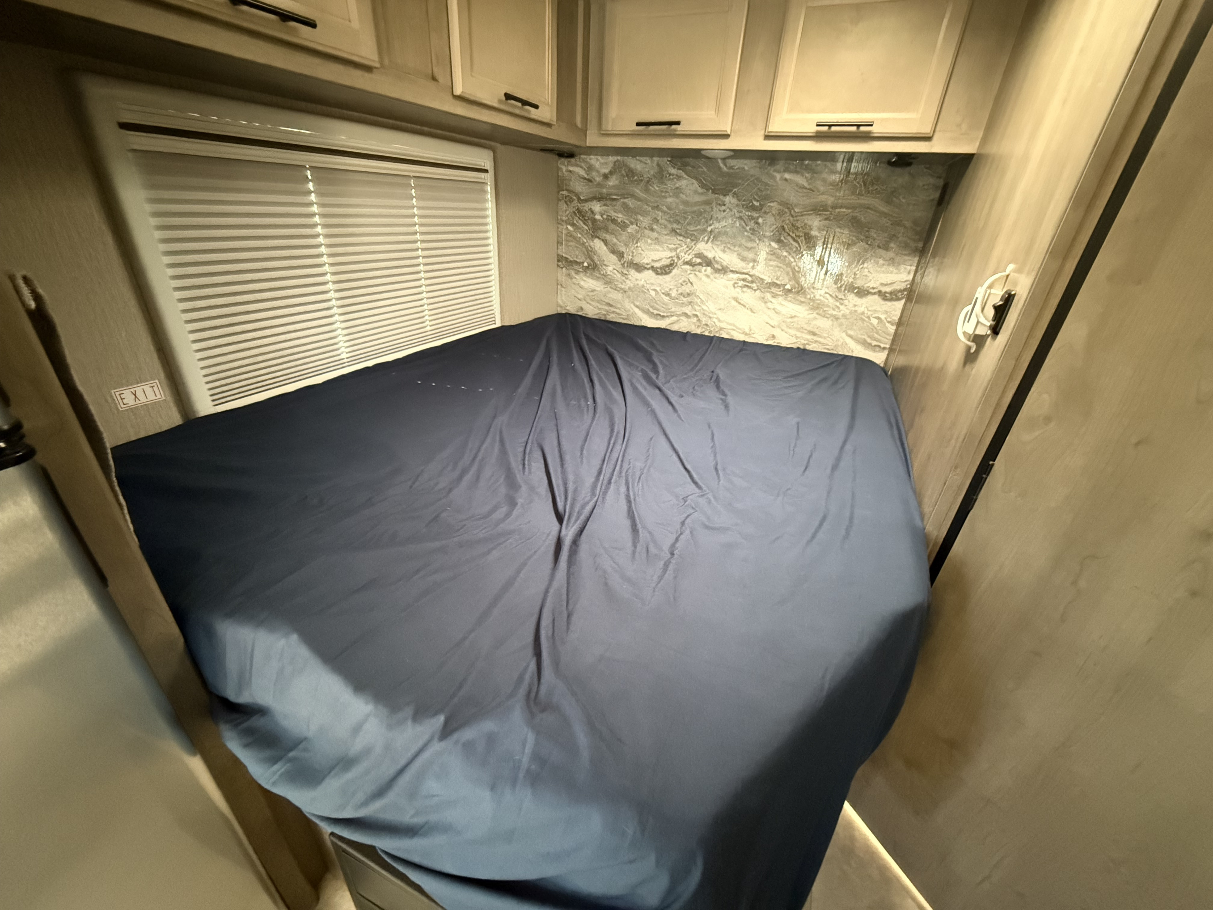 RV rental bedroom: dark blue bed, marbled wall, window blinds, and overhead cabinets for a comfortable stay.. 1HAGGUC78MN008793 Cross Trail 2022