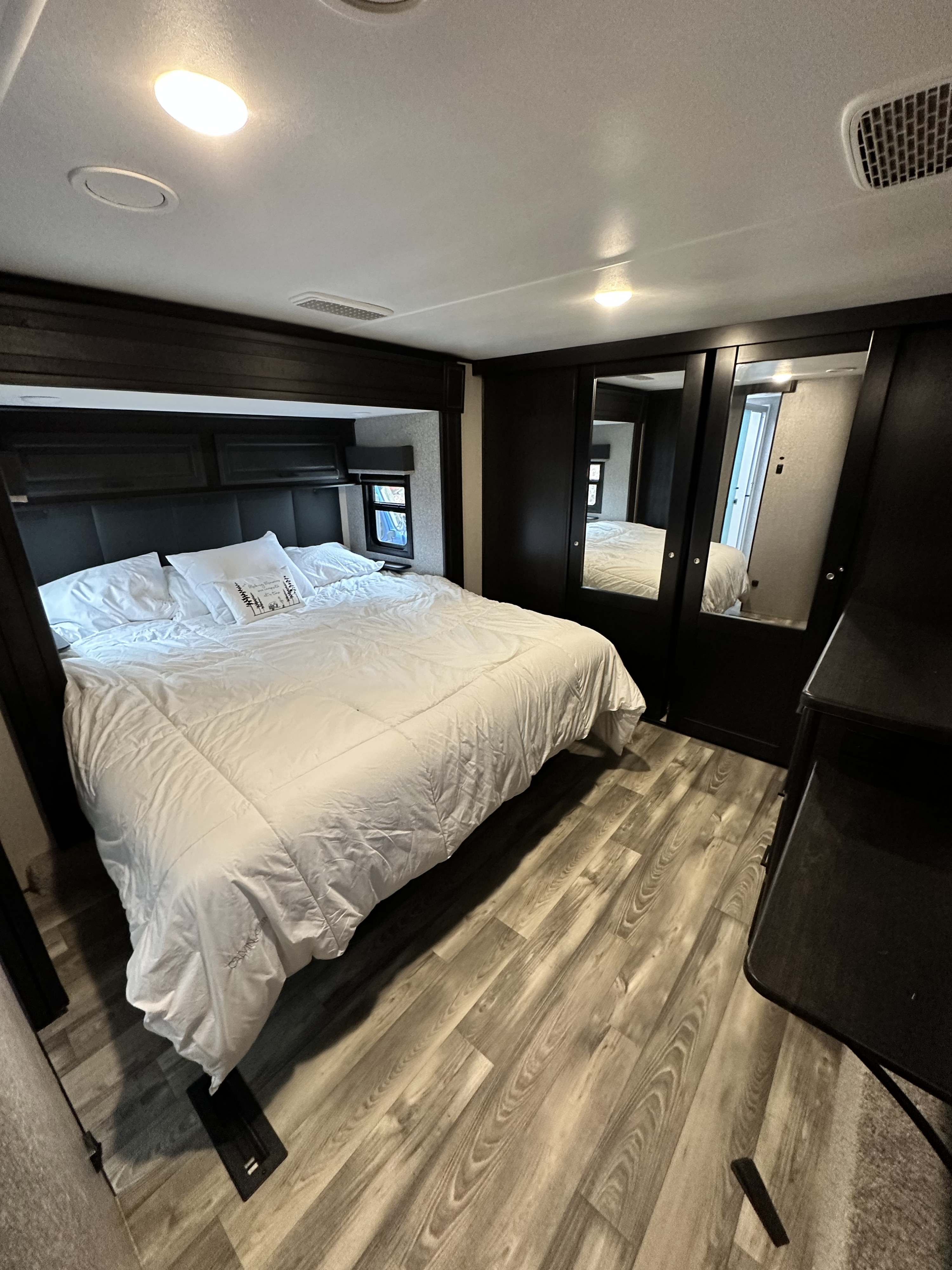 Spacious RV rental bedroom featuring a comfortable bed with white bedding, modern dark wood cabinetry, and laminate flooring.. Highland Ridge RV Open Range 2022